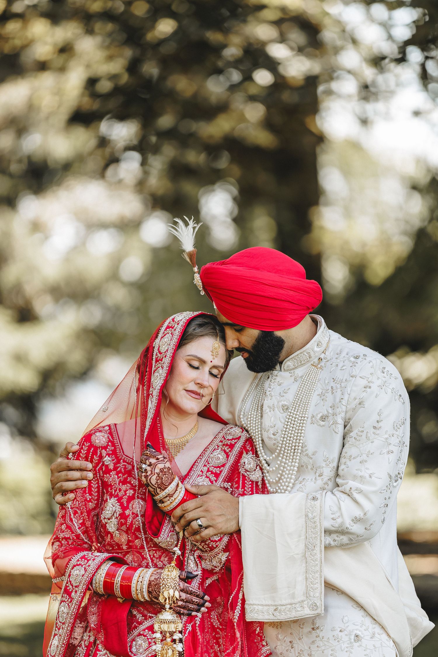 A couple in traditional Sikh wedding attire sharing an intimate moment outdoors.