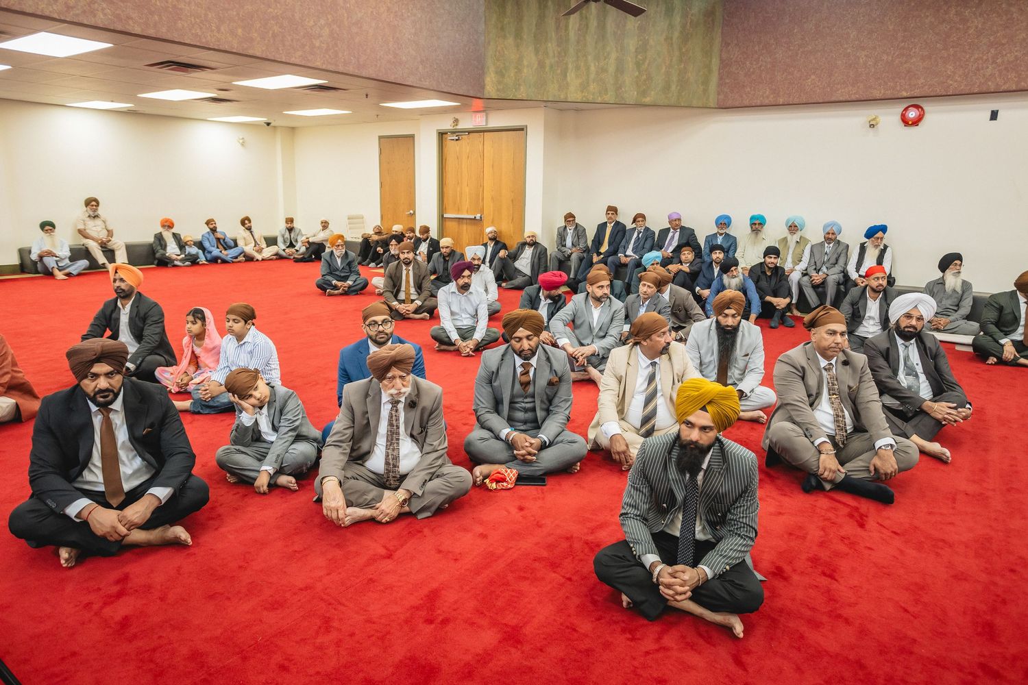 A group of people sitting cross-legged on red carpet in a large meeting room during a gathering.