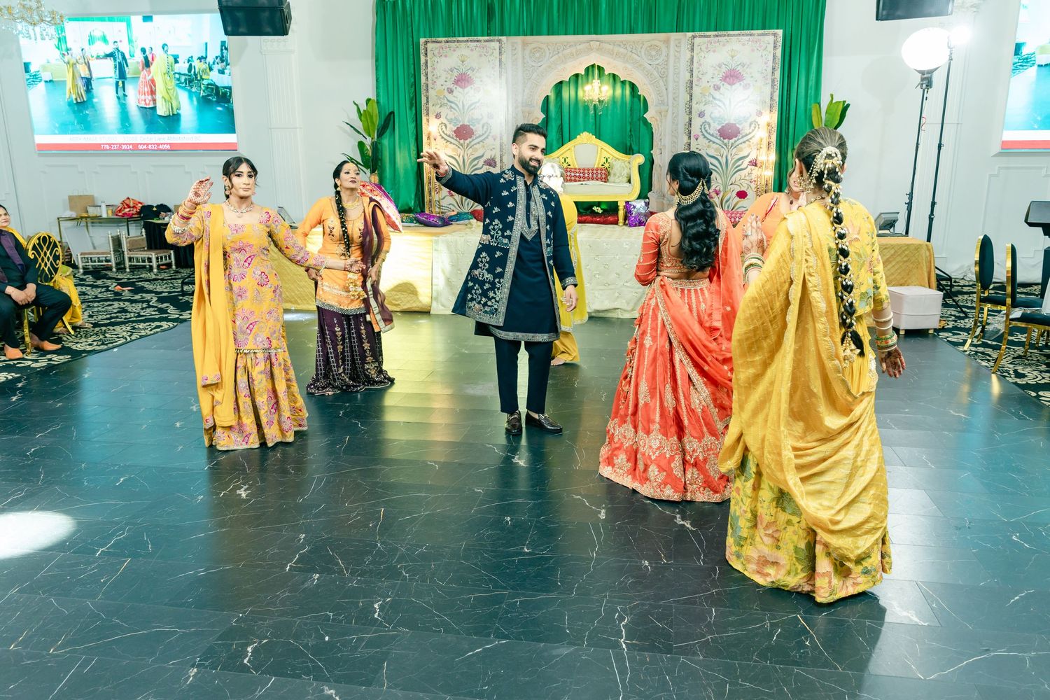 Traditional Indian dancers in bright yellow and red outfits perform on stage with green curtains.