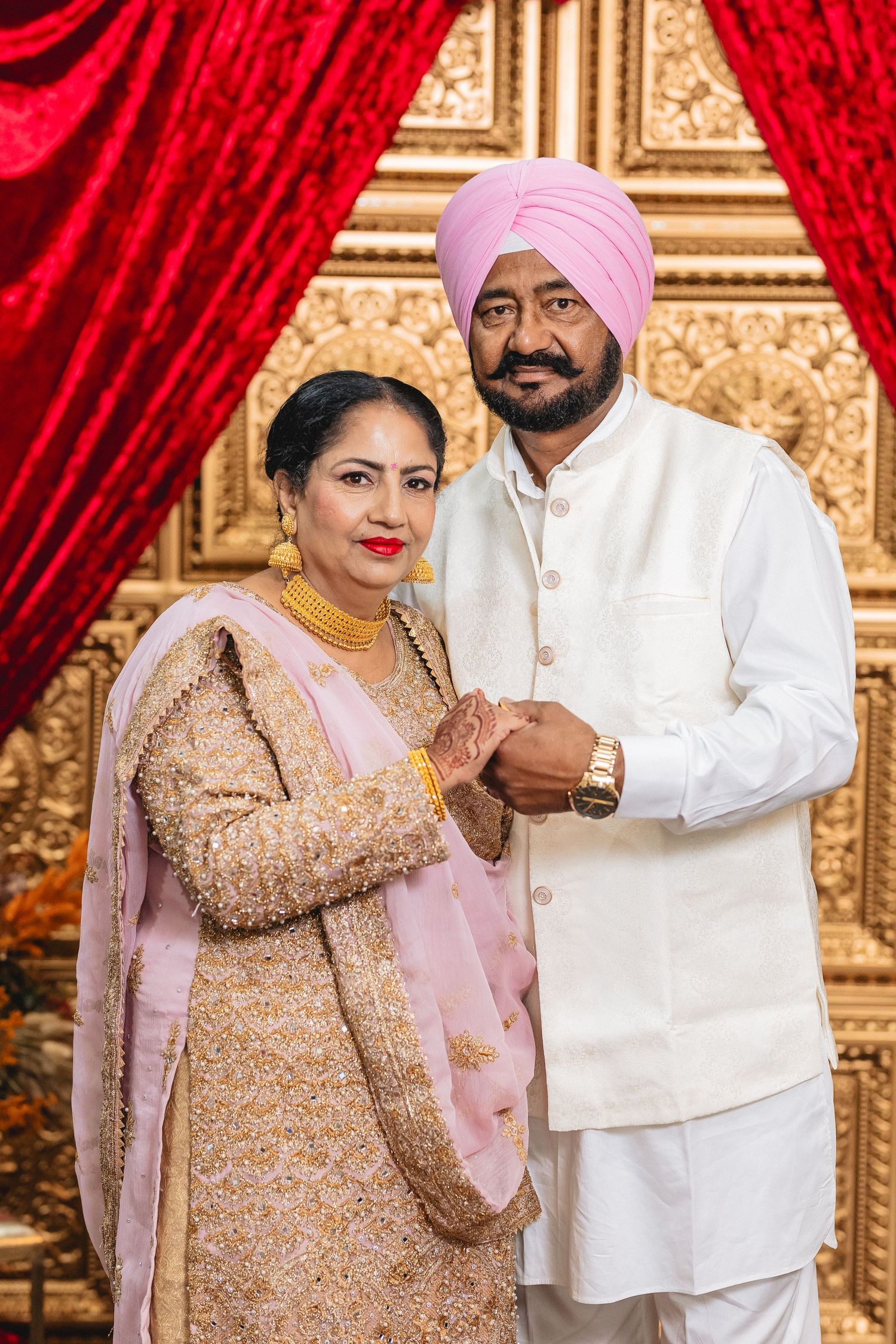 Traditional Punjabi wedding ceremony with red velvet curtains and gold decorative backdrop.