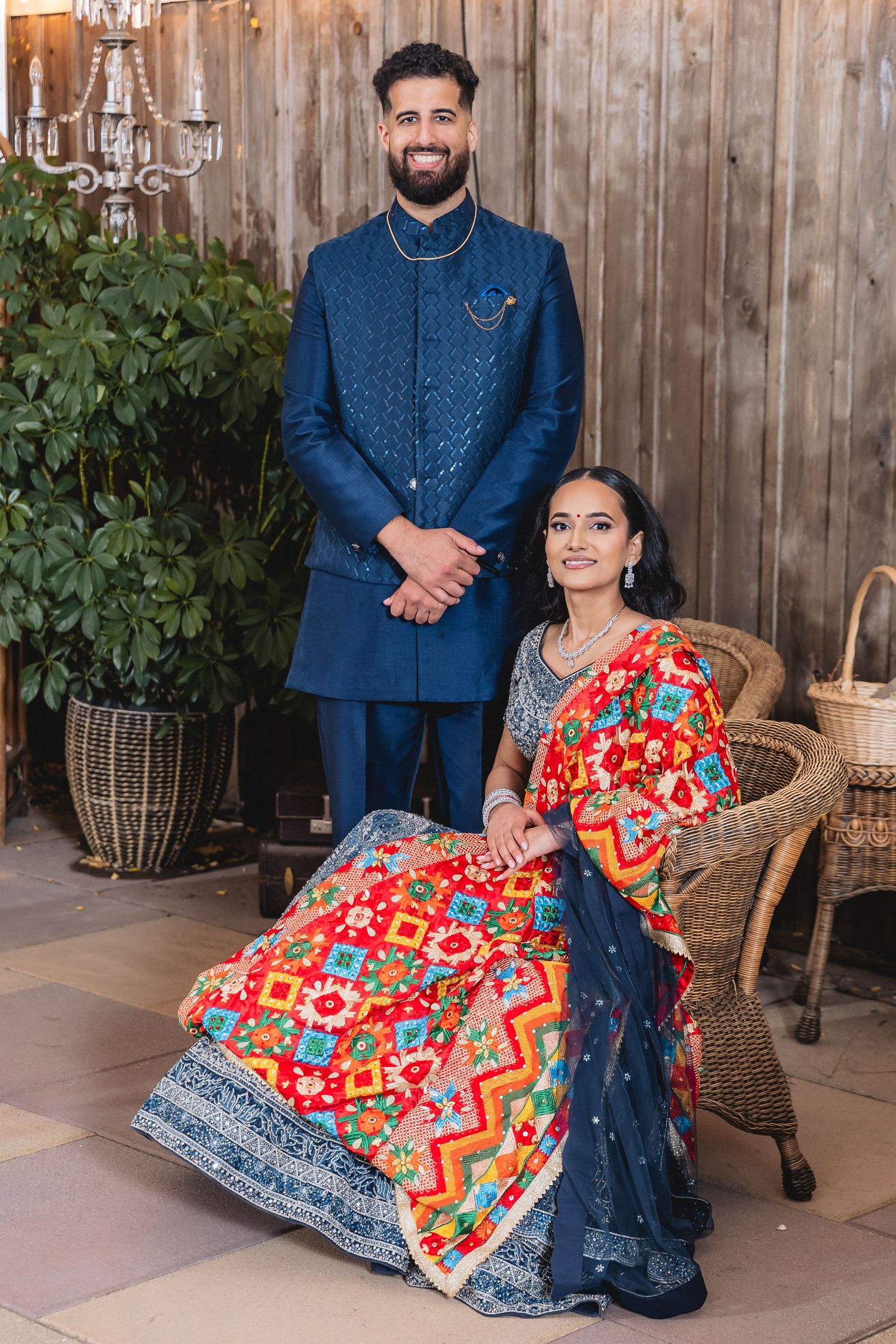 A couple in coordinated blue and red outfits pose for engagement photos on a wooden deck. Studio Portraits at Engagement ceremony.