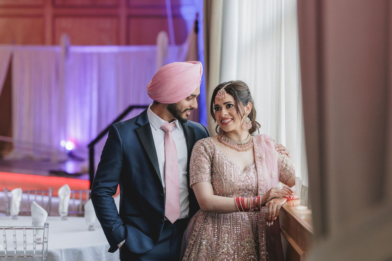 Wedding celebration in an elegant ballroom with pink and purple mood lighting.