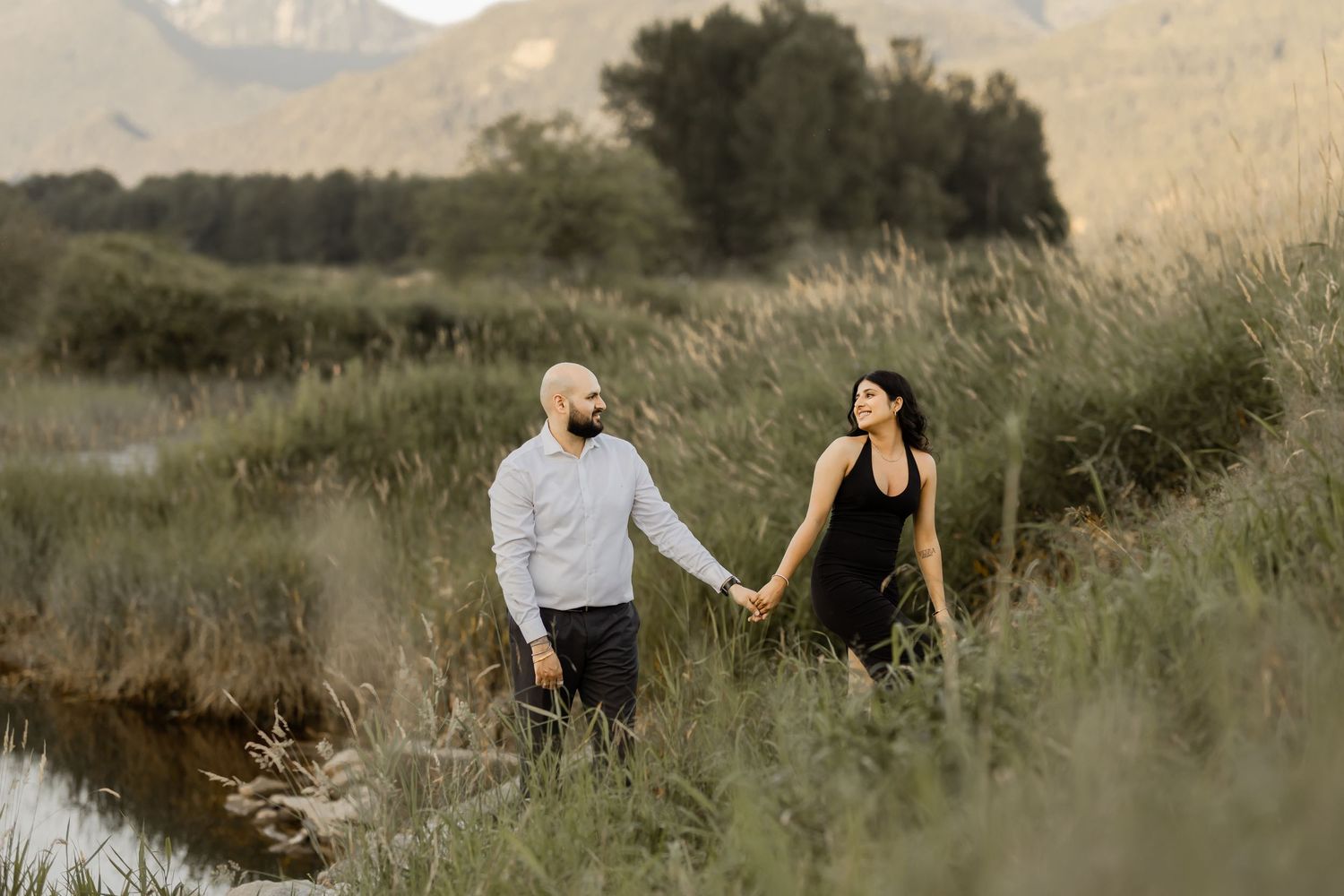 A couple walks hand in hand through a scenic mountain meadow during their engagement session.