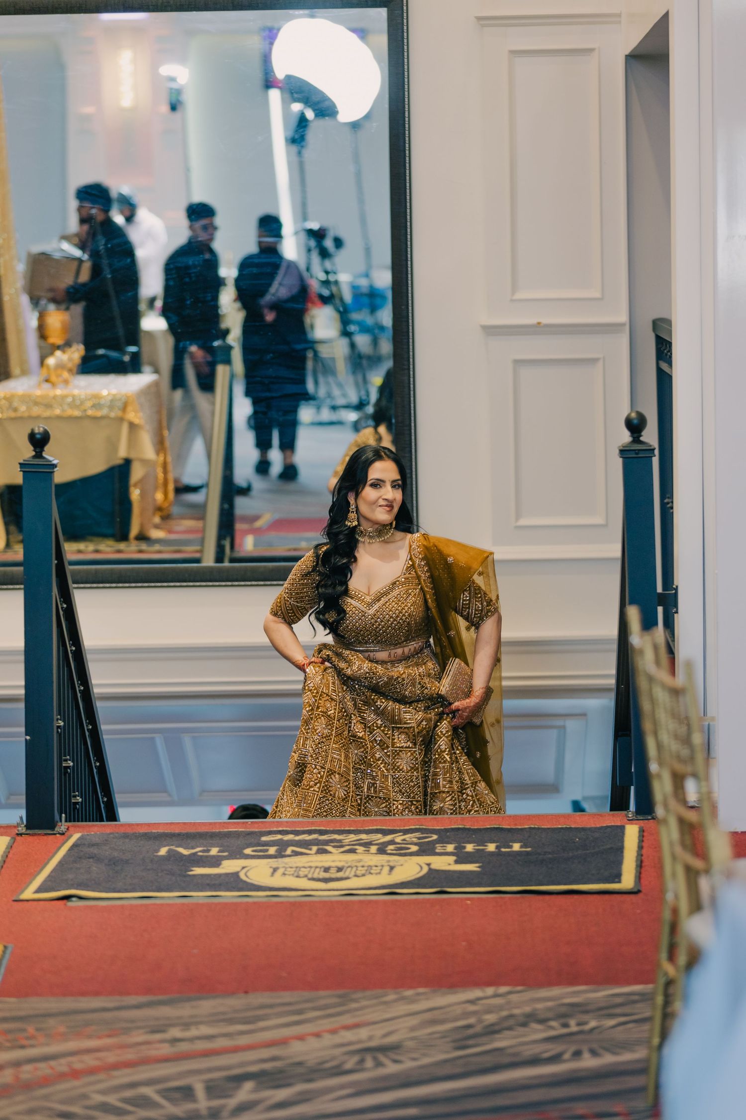 Ornate gold lehenga dress displayed on a raised platform with elegant white wall panels.