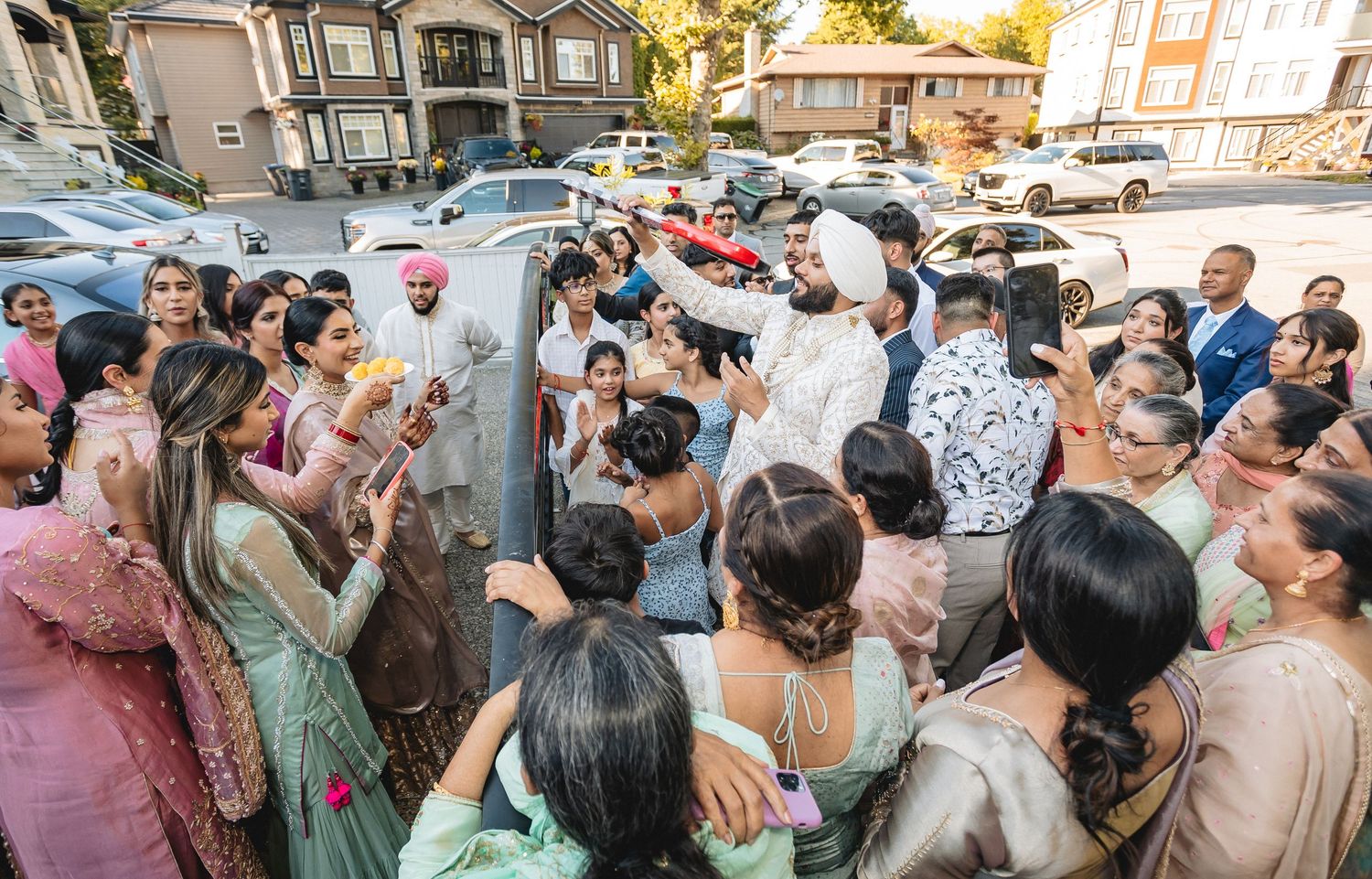 Large crowd of wedding guests gathered outside taking photos and videos with phones raised.