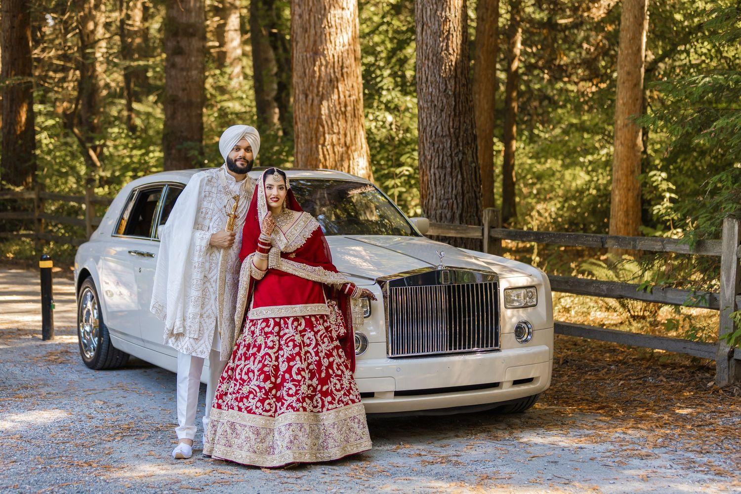 Wedding party posing for photos in a wooded outdoor setting with luxury cars in the background.