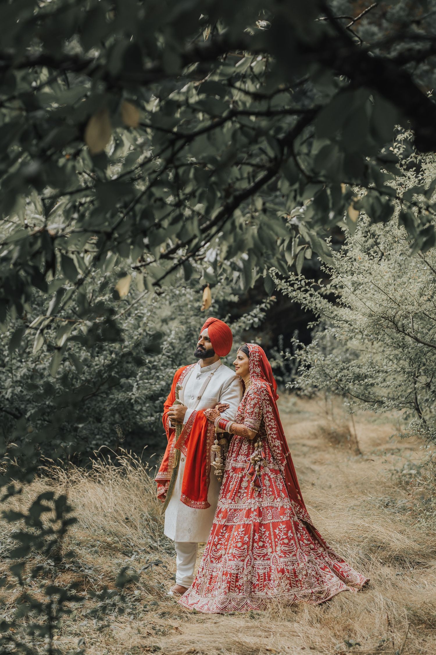 Couple in traditional Indian wedding attire walking through a scenic outdoor setting.