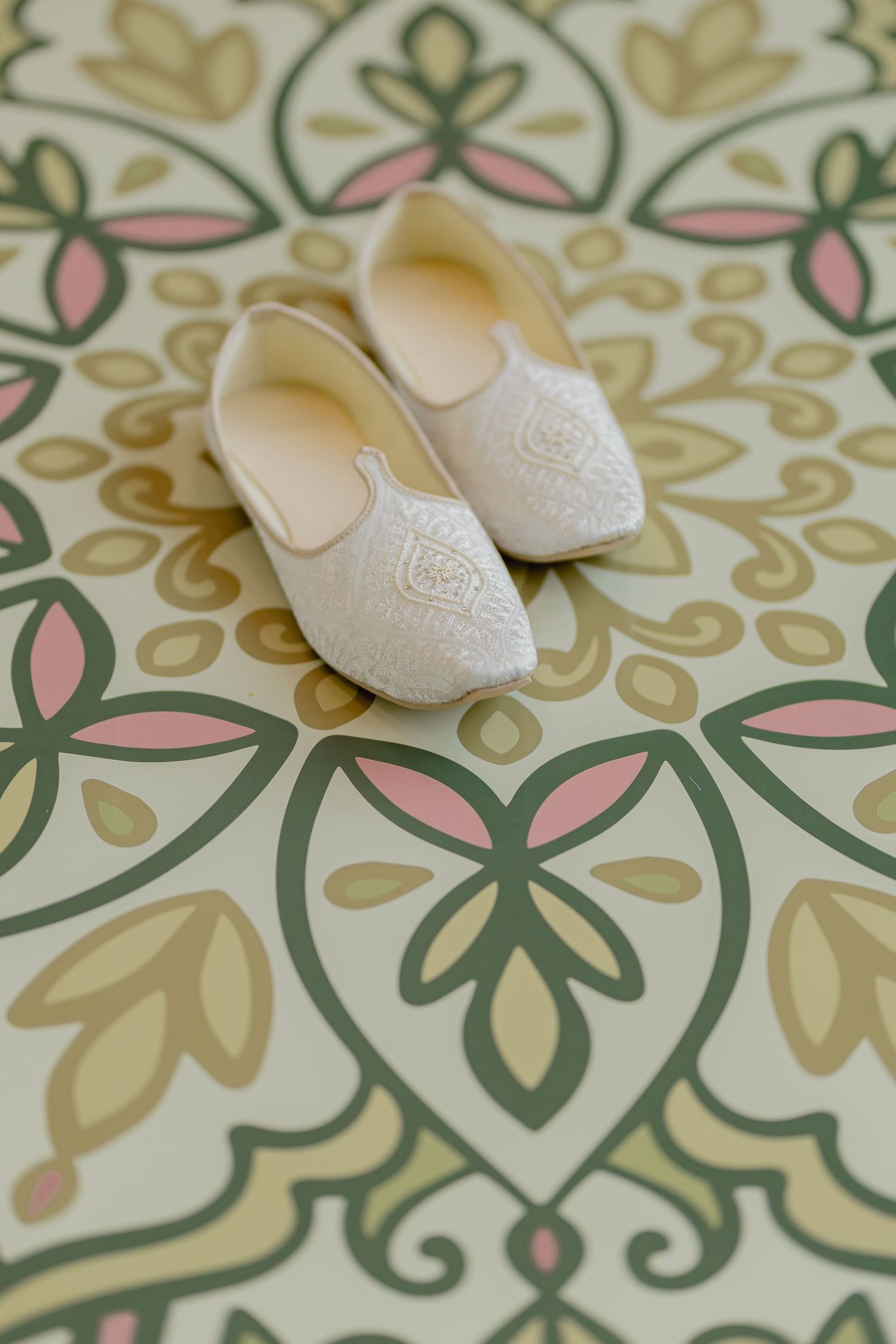 White traditional mojari shoes photographed on geometric floral patterned background.
