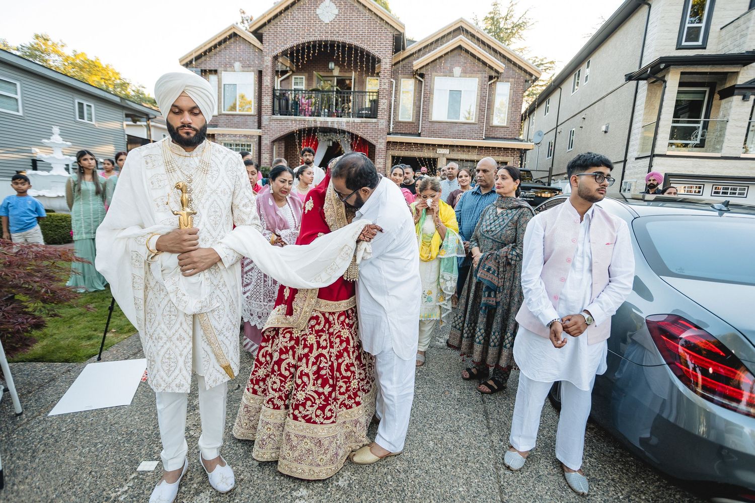Wedding party members in white traditional attire walking along a street.