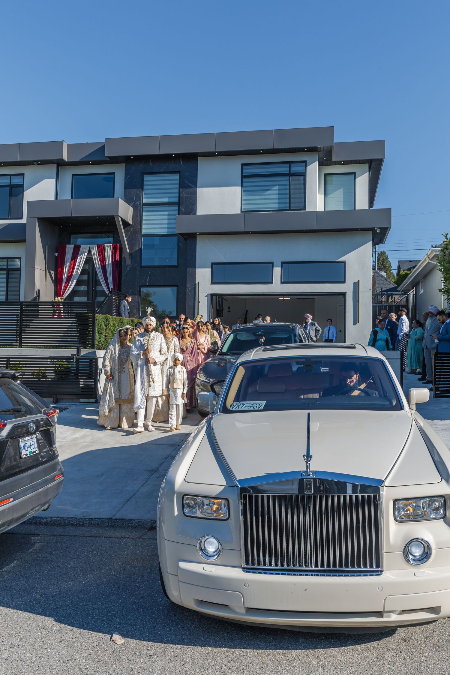 A white Rolls Royce luxury car parked in front of a modern building during a wedding celebration.