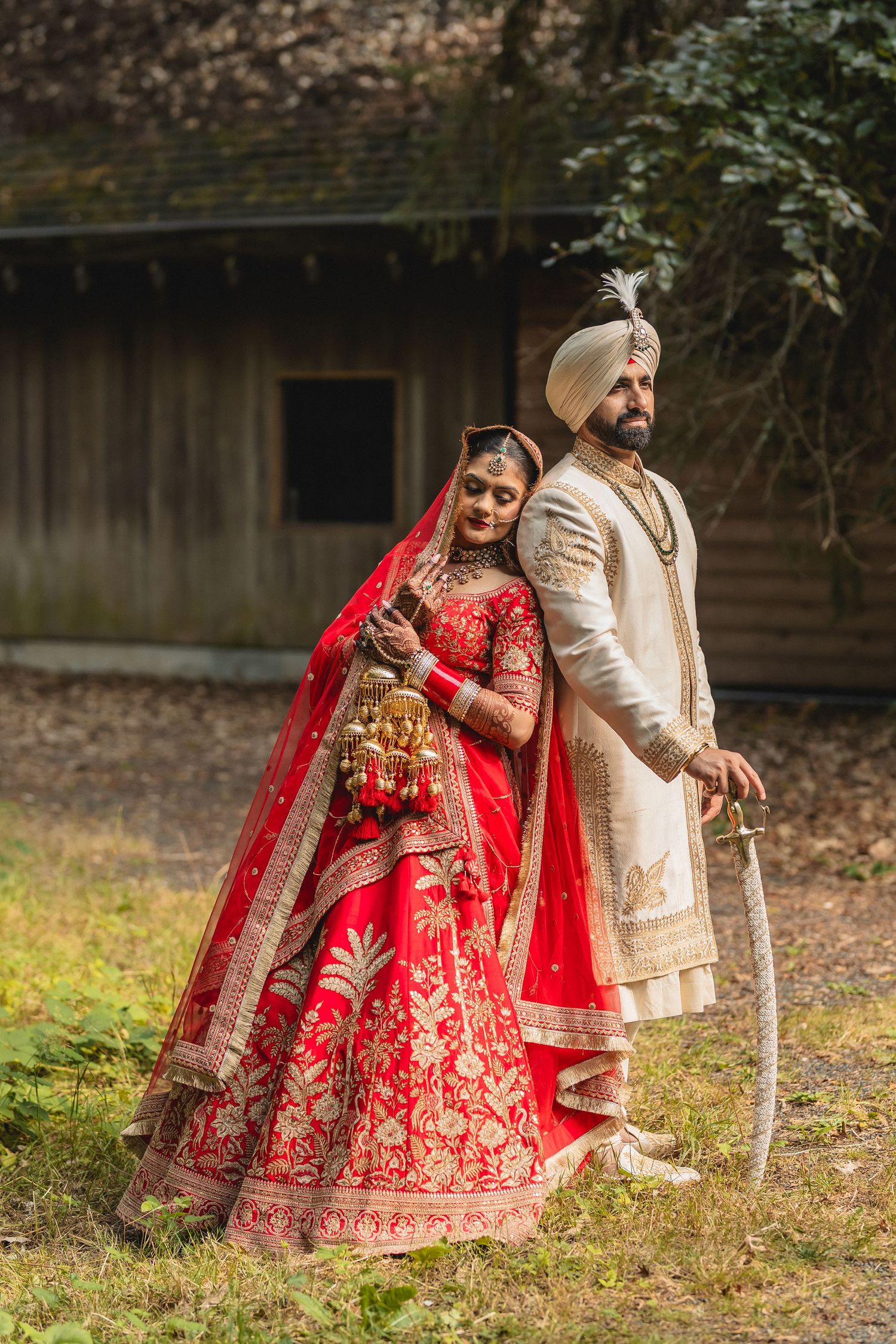 Couple in traditional Indian wedding attire poses outdoors in wooded setting.