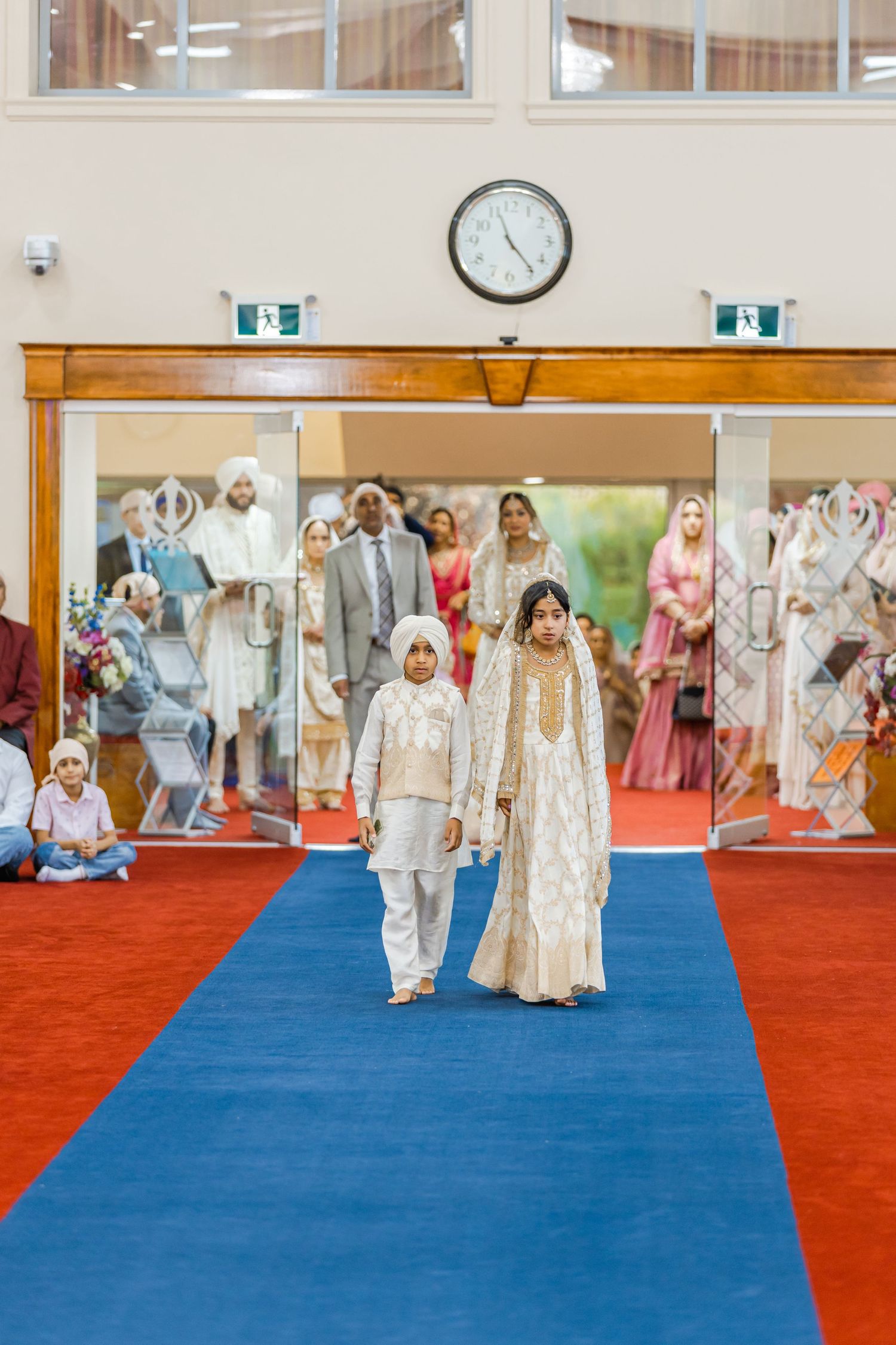 Wedding ceremony procession on a blue carpet runner with red carpeting on the sides.