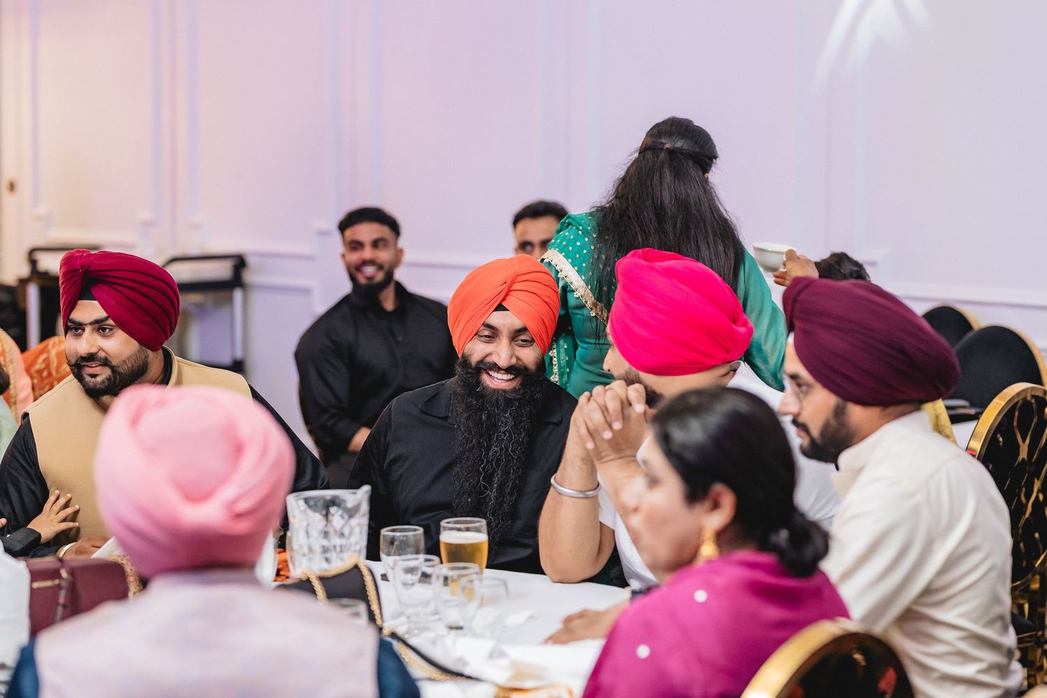 Wedding guests in traditional Sikh attire seated at round tables during a reception celebration.
