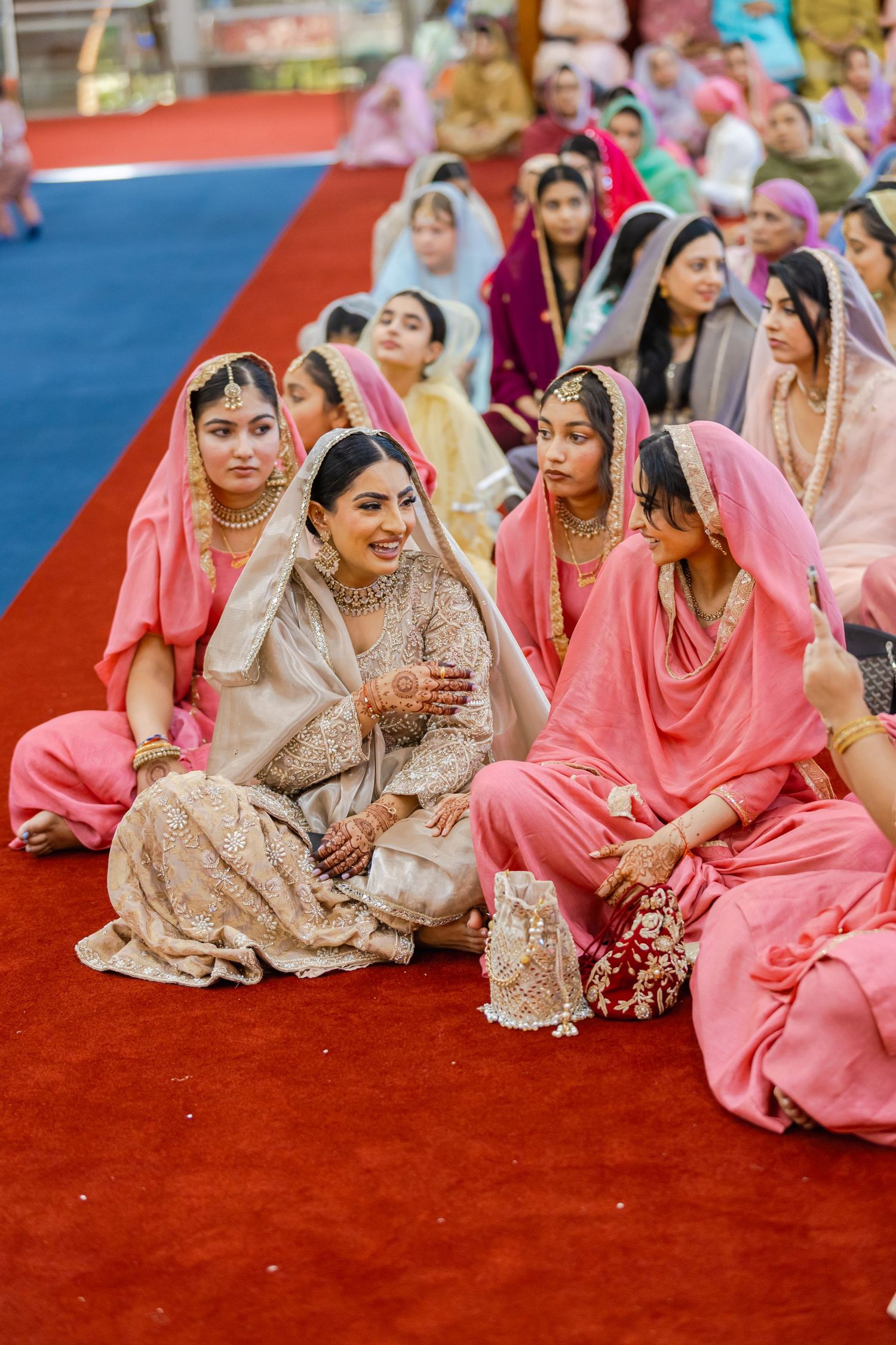 Women in colorful traditional attire seated on floor during Indian wedding ceremony.