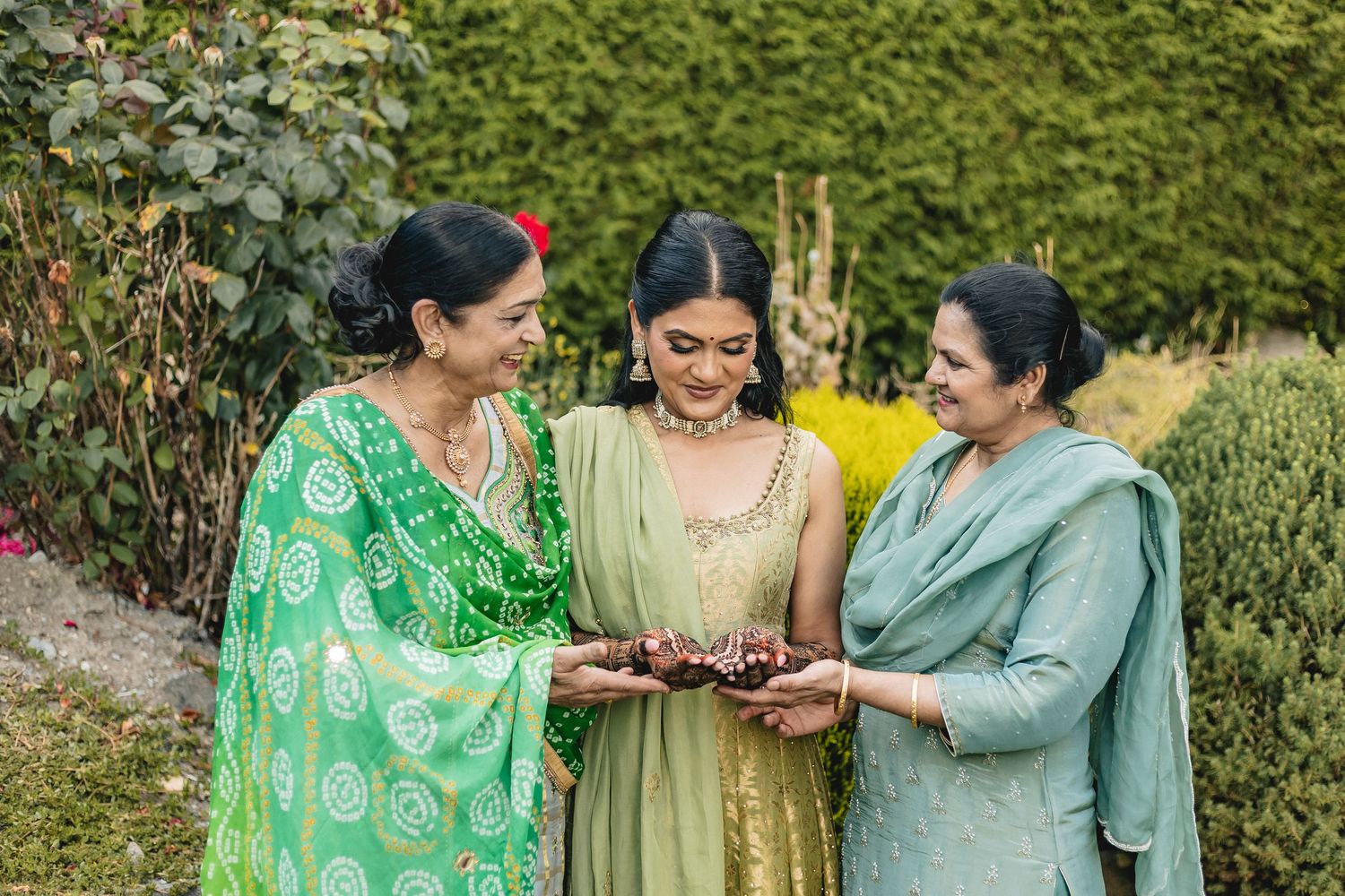 A group of women in traditional Indian attire share joyful moments together in a garden setting.