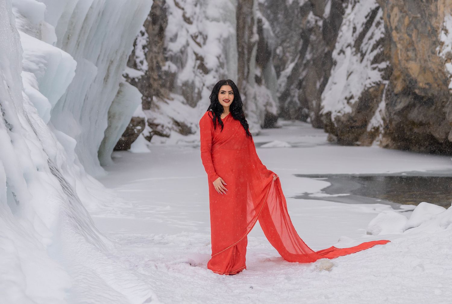 Woman in red gown poses gracefully among snow and ice formations in a winter landscape.