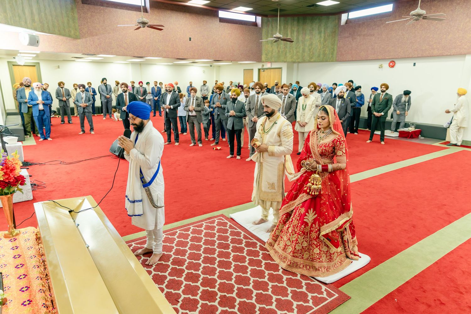 Wide angle view of wedding ceremony in hall with red carpet and standing guests.