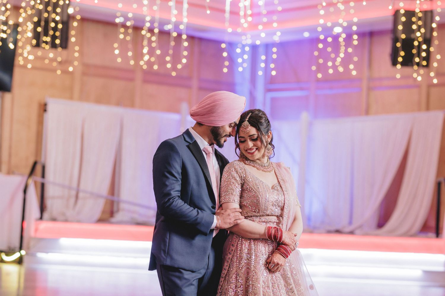 Romantic wedding reception venue illuminated with string lights and purple ambient lighting.