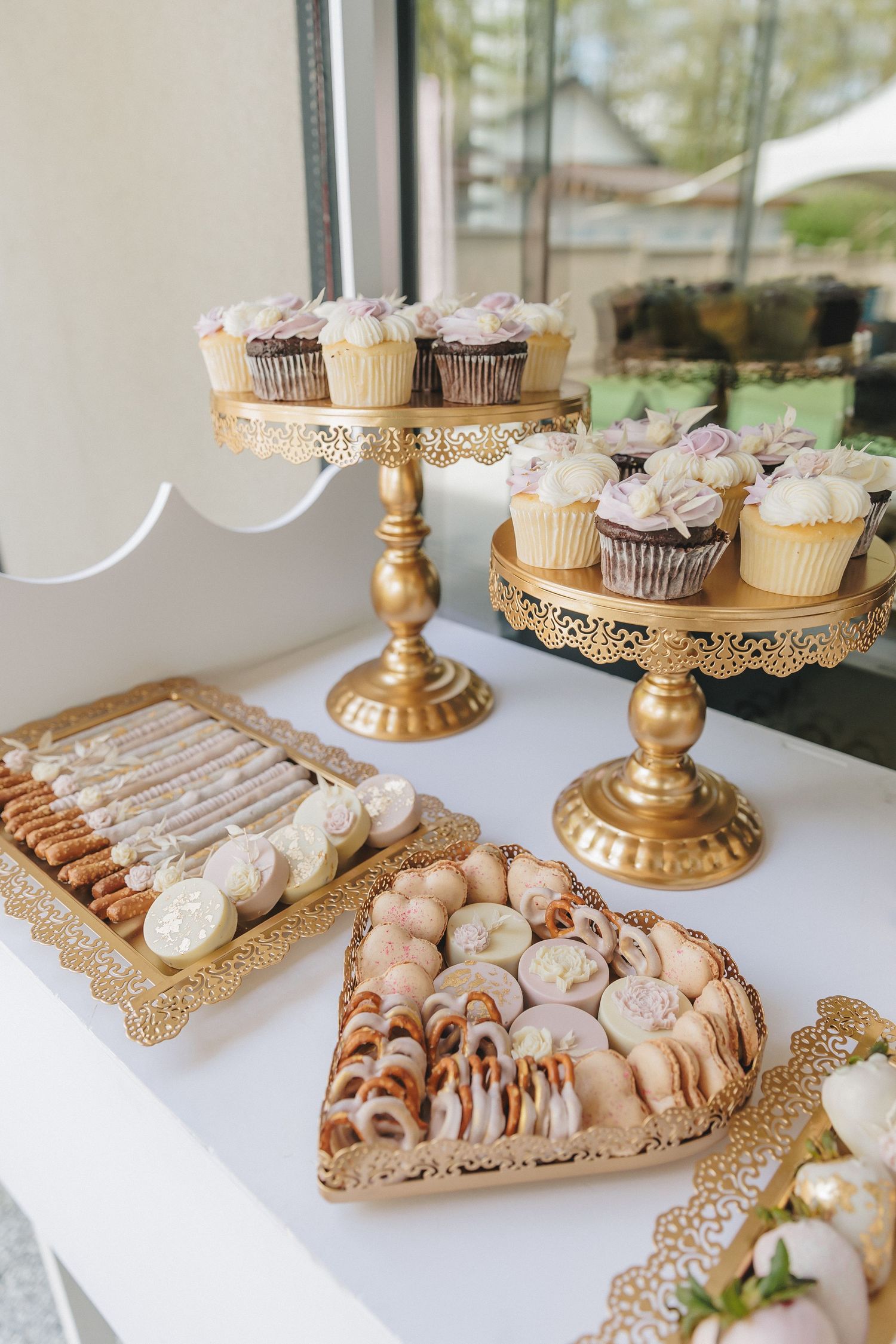 Gold cake stands displaying an assortment of desserts and pastries on a white tablecloth.