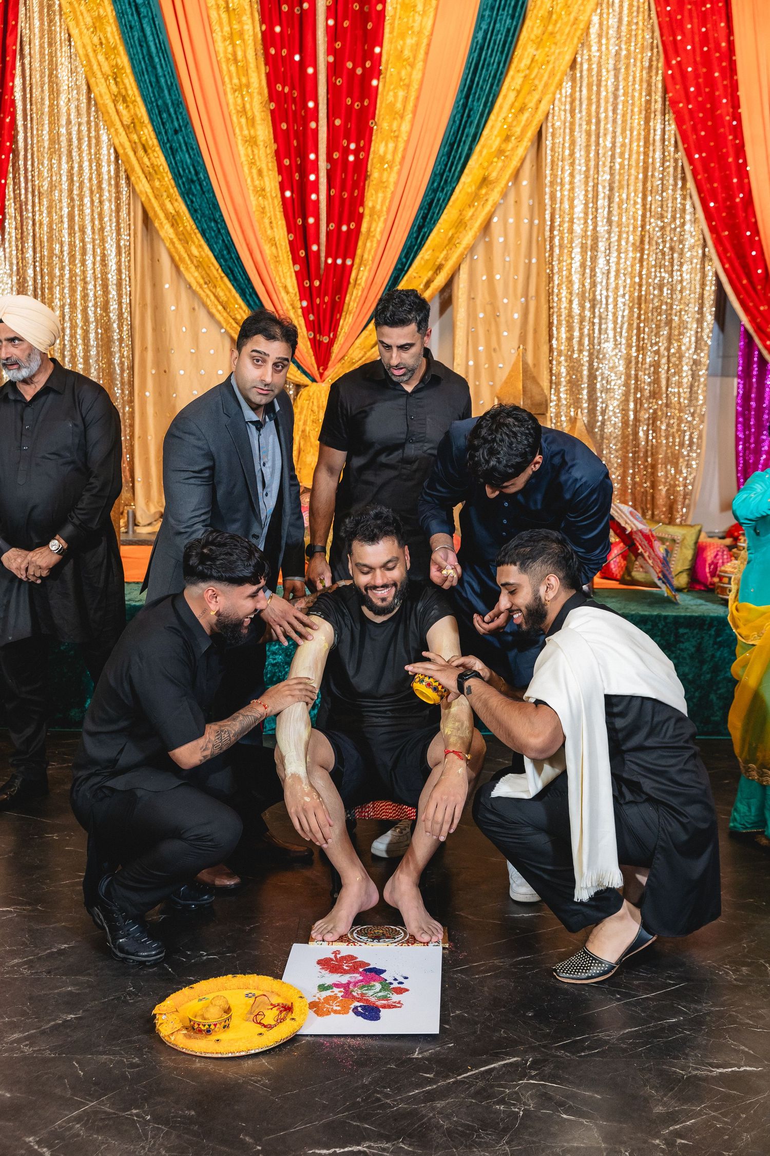 Group performing traditional wedding rituals with colorful decorations and golden backdrop.