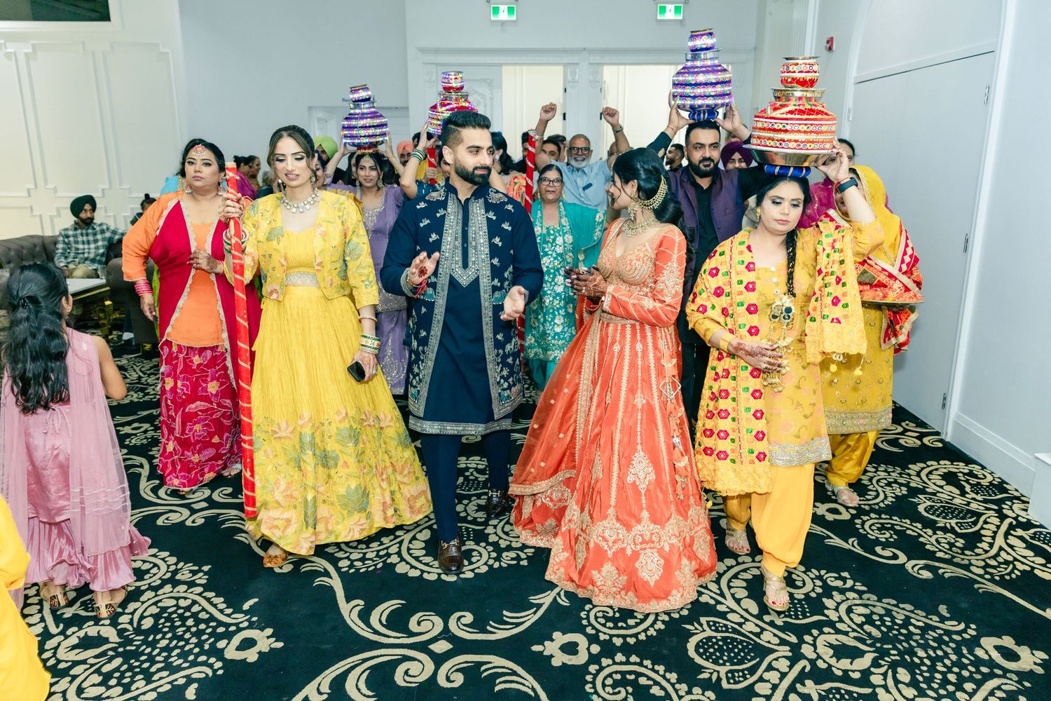 Guests in colorful traditional Indian attire dance and celebrate at an indoor wedding reception.