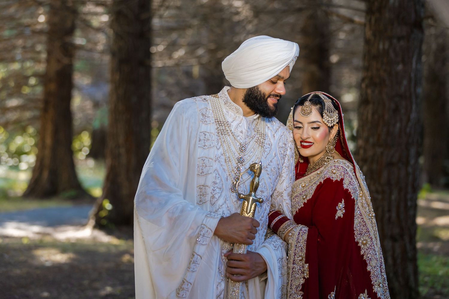 Traditional Sikh wedding couple sharing an intimate moment in a wooded setting.