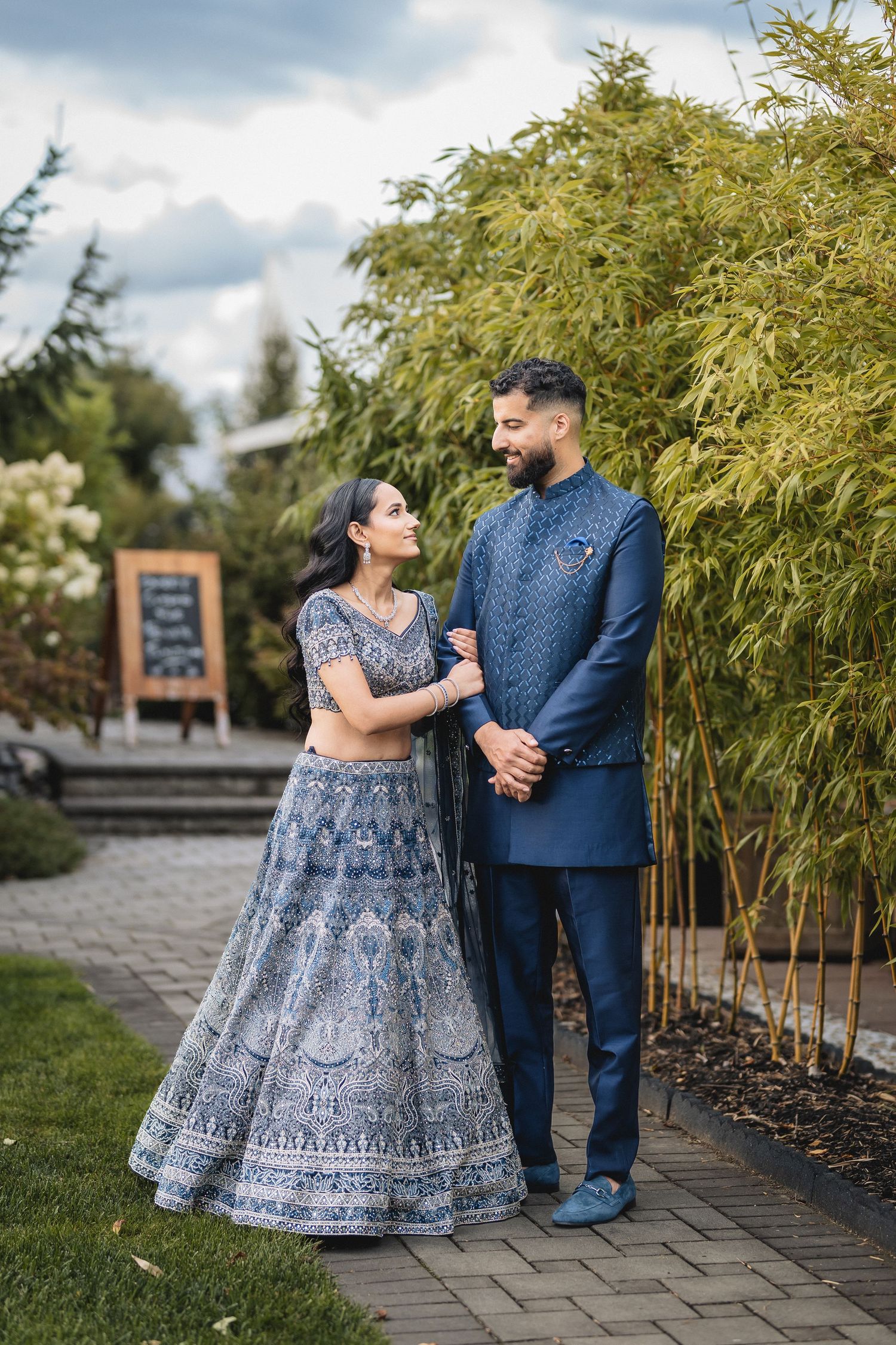 Couple in blue and gray traditional outfits pose together near bamboo garden.