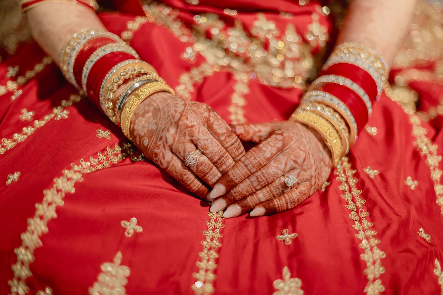 Close-up of hands adorned with gold bangles and traditional jewelry on red fabric.