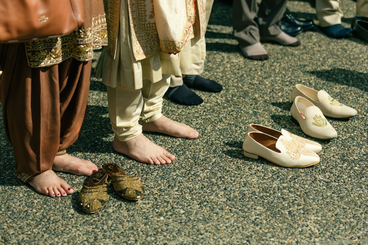 Detail shot of traditional footwear and bare feet on gravel ground at Indian wedding.