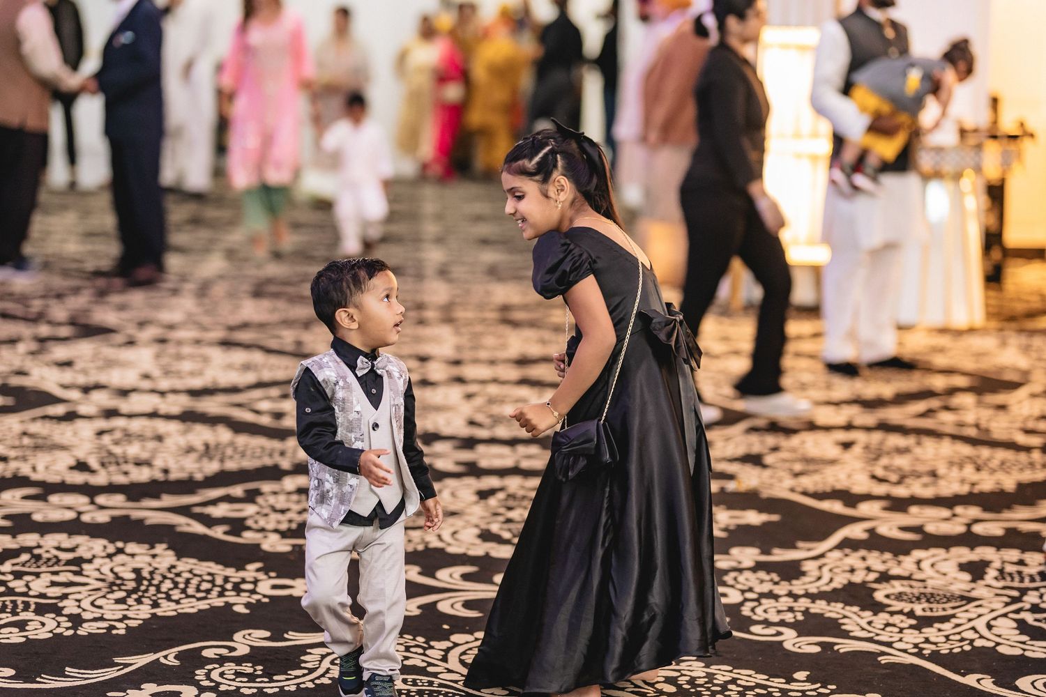 Guests in formal attire gather on an ornately patterned floor at an elegant event.