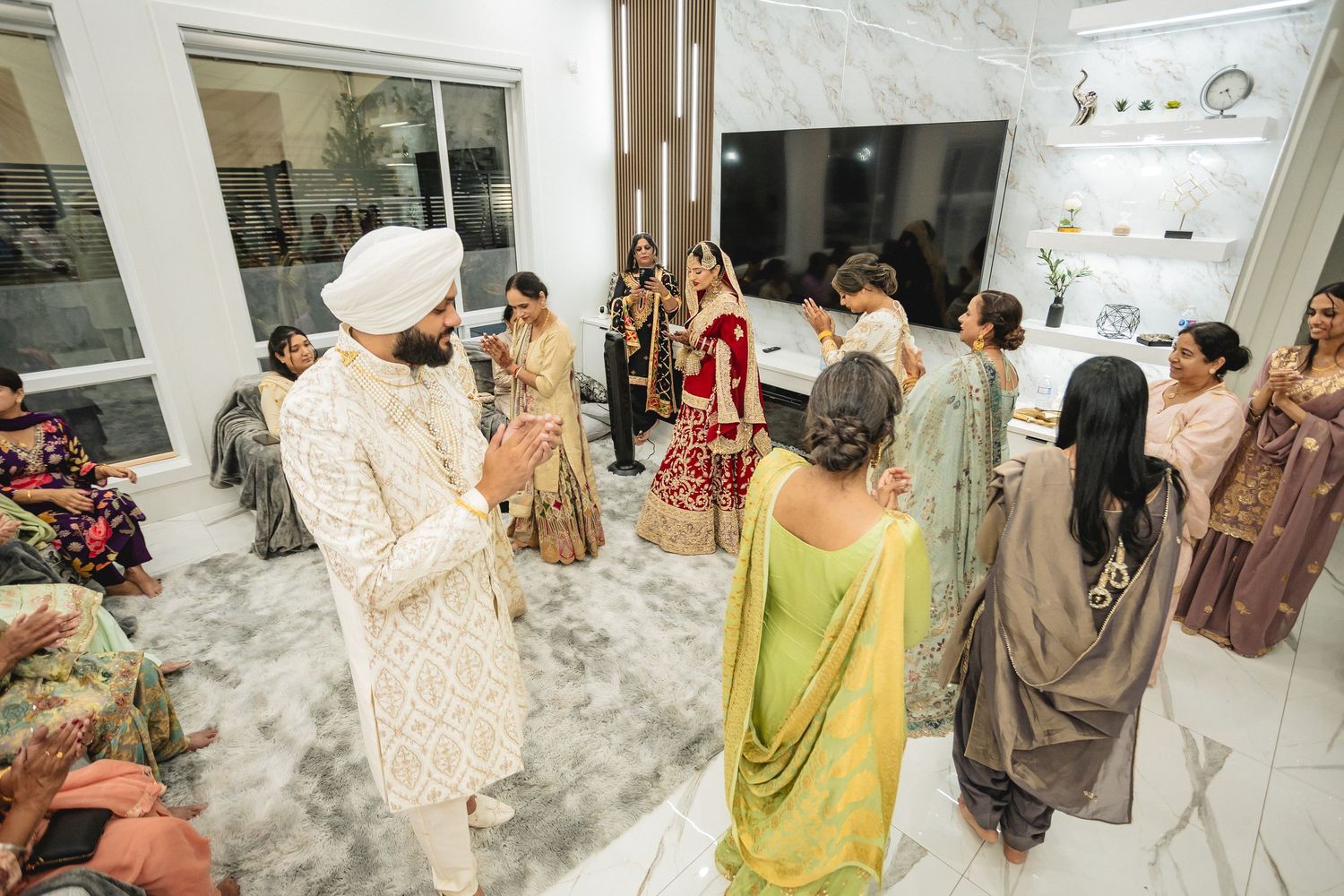 Guests in formal attire mingle and socialize at an elegant indoor event venue with white decor and lighting.