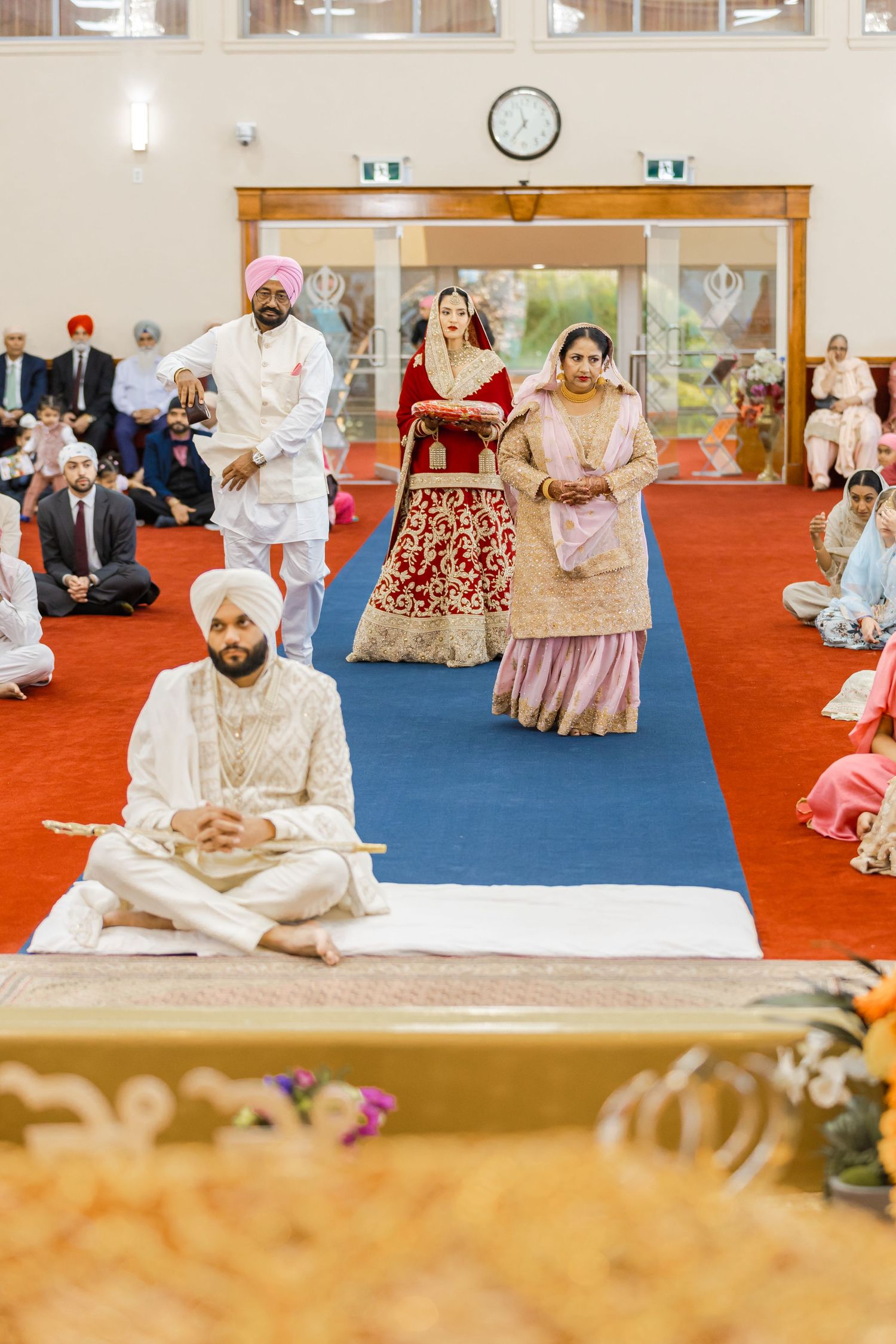 Traditional Sikh wedding ceremony taking place in a temple with guests seated on floor.