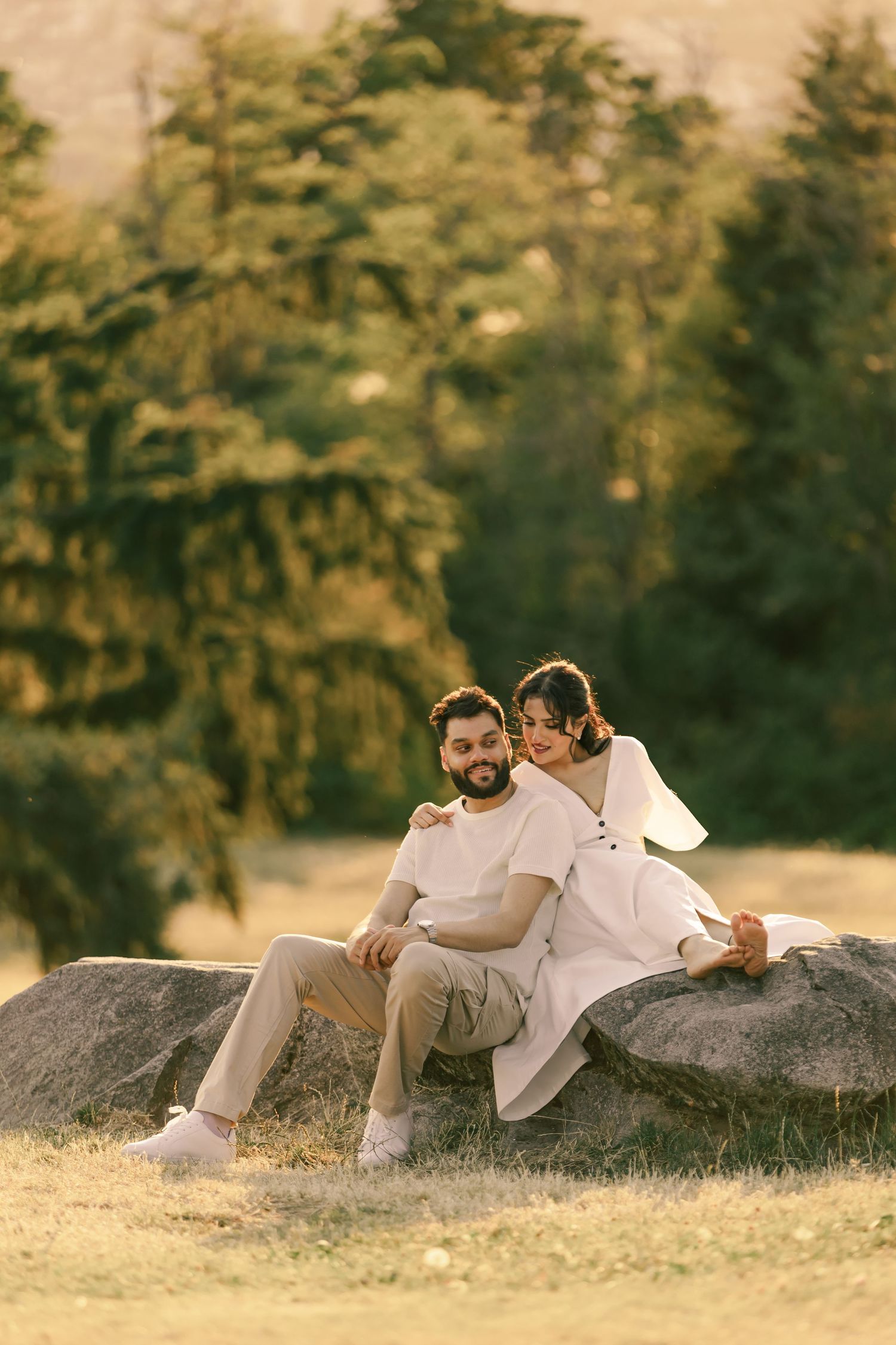 A couple lounges intimately on a large boulder during a golden sunset in nature.