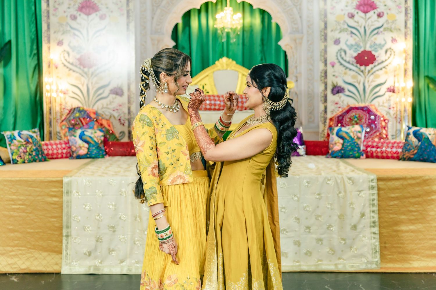Two people in matching yellow outfits embrace at traditional Indian ceremony venue.