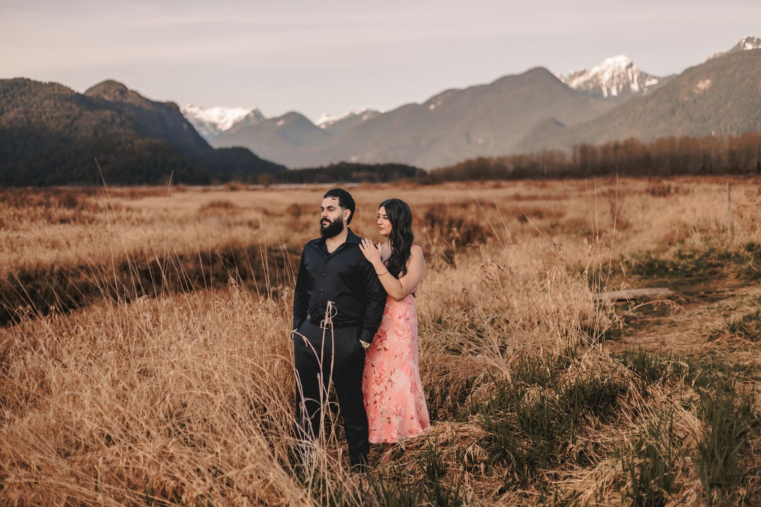 A romantic mountain landscape photoshoot with snow-capped peaks and golden grass in the foreground.