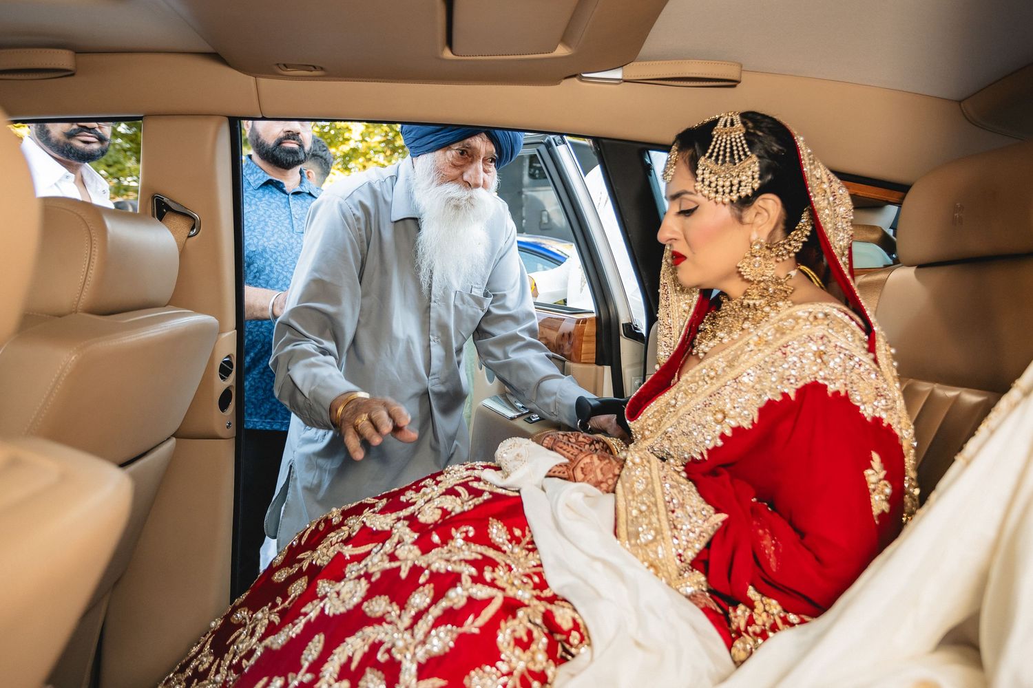 A bride in a traditional red wedding lehenga sits in a luxury car interior.