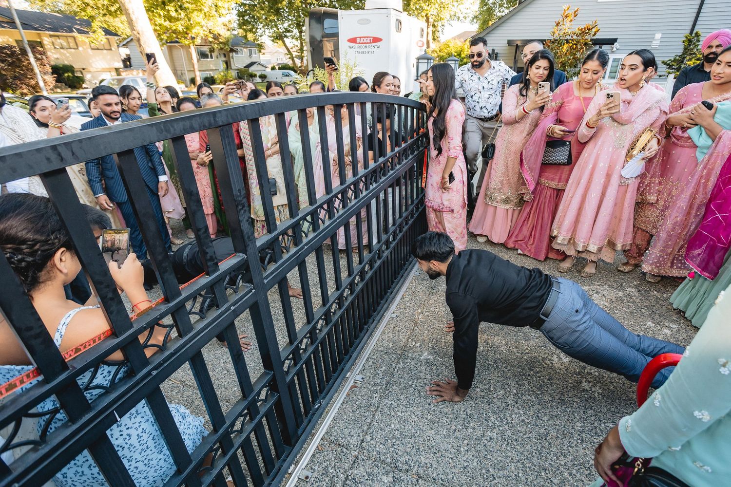 A photographer lies on the ground to capture a creative shot of wedding guests through decorative railings.