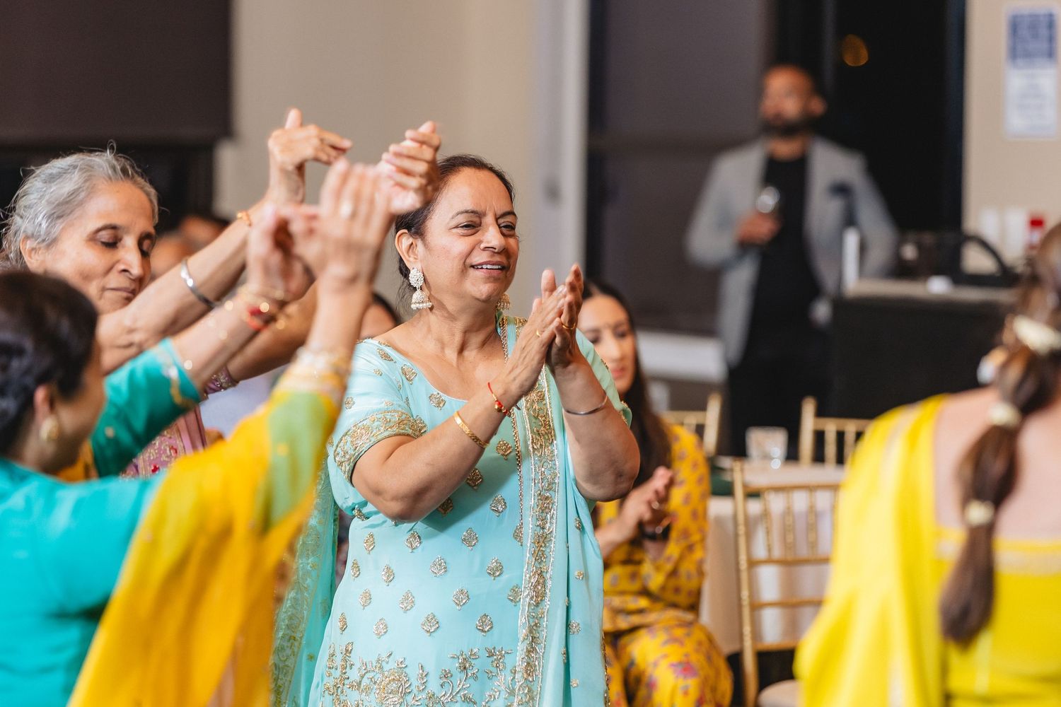 People in yellow and turquoise outfits dance and celebrate together at an indoor event.