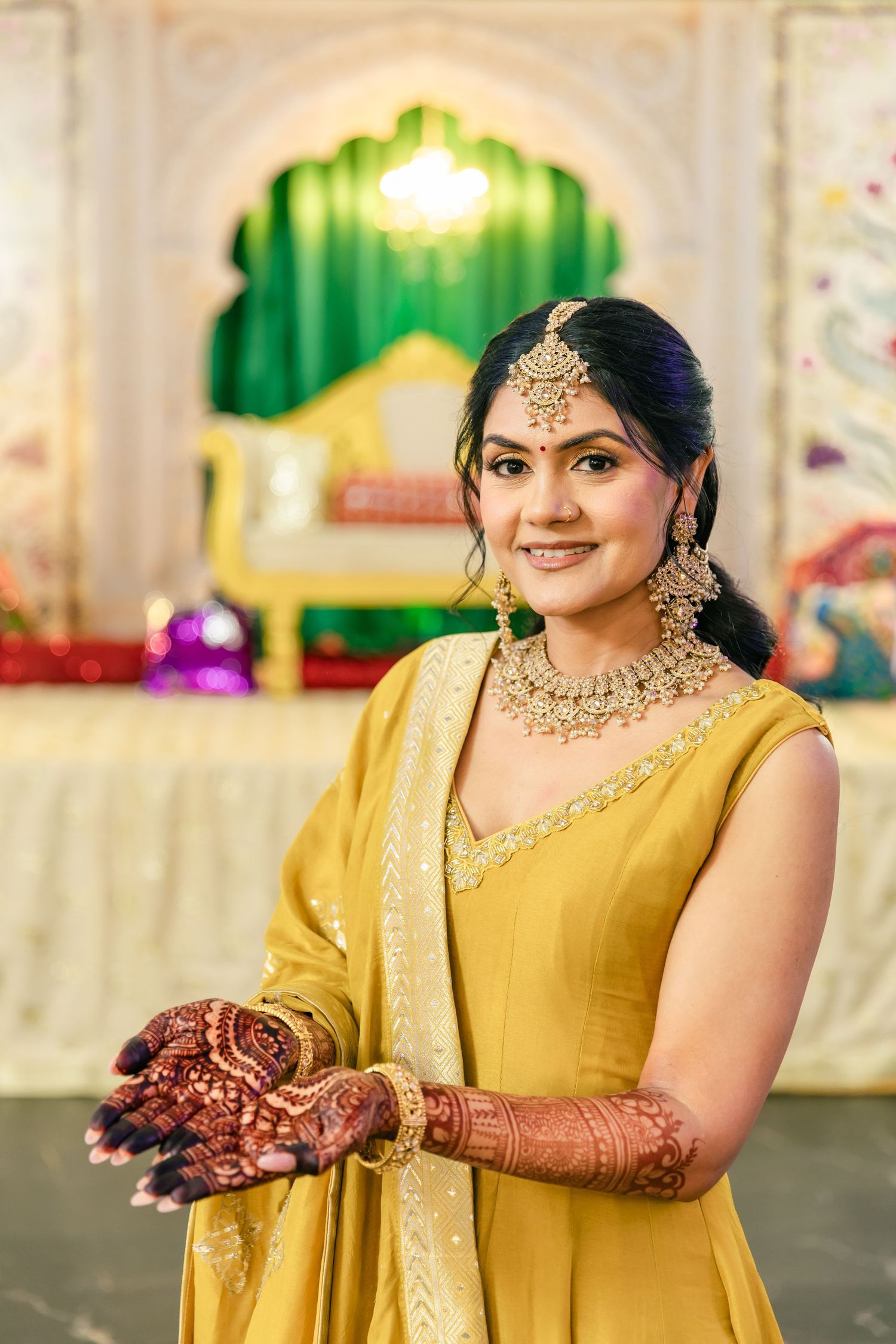 Person in yellow traditional Indian dress shows intricate henna designs on hands during wedding ceremony.