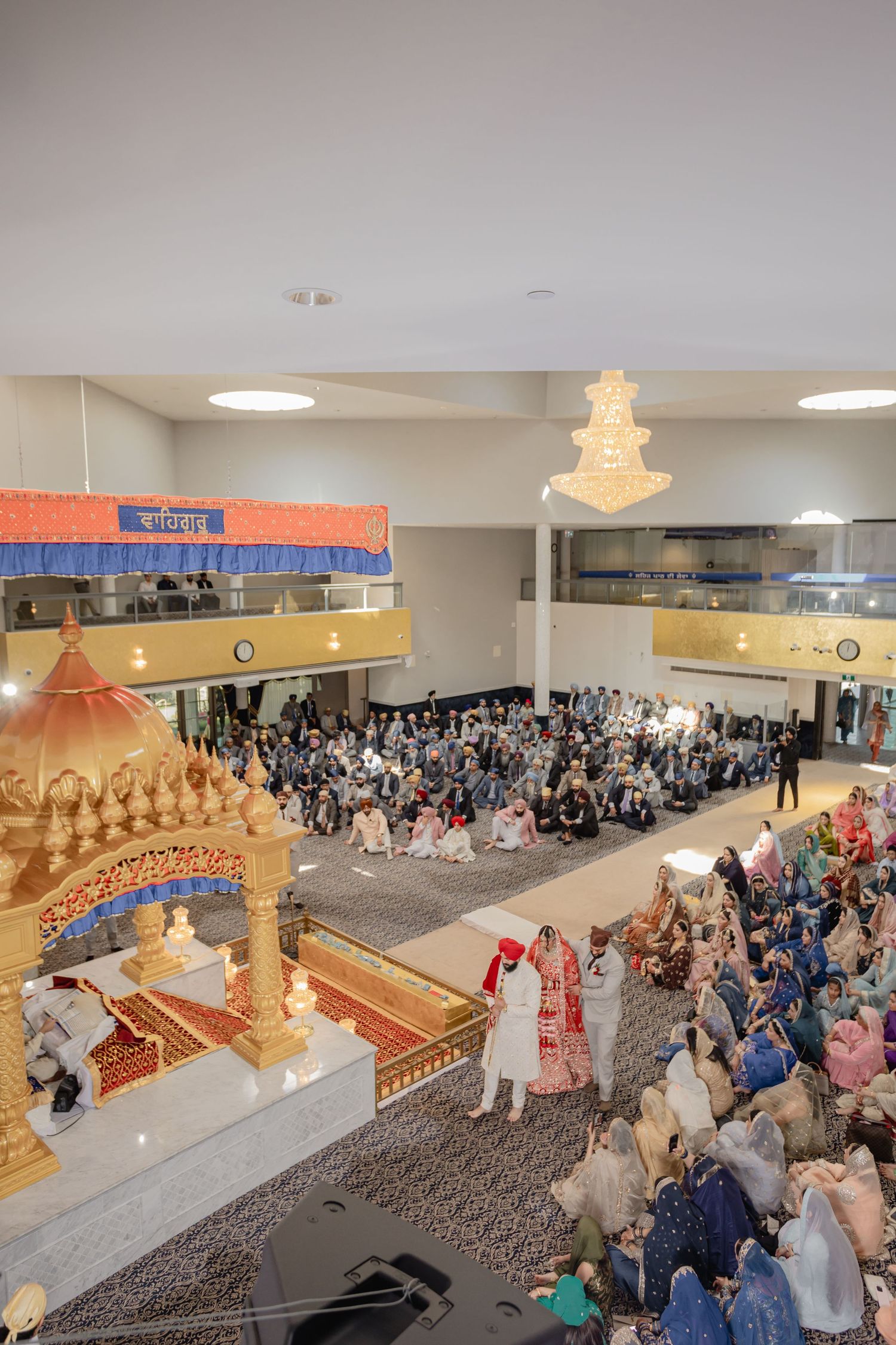 Large indoor cultural ceremony with elevated stage and gathered audience members.