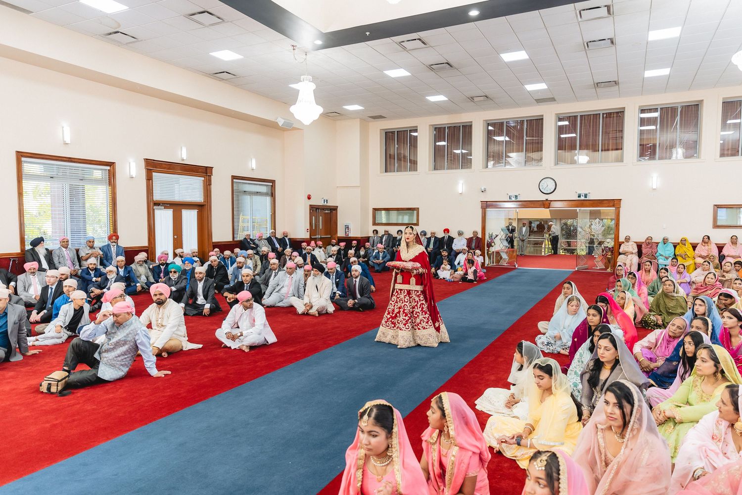 Large gathering hall with red carpeting and attendees seated during ceremony.