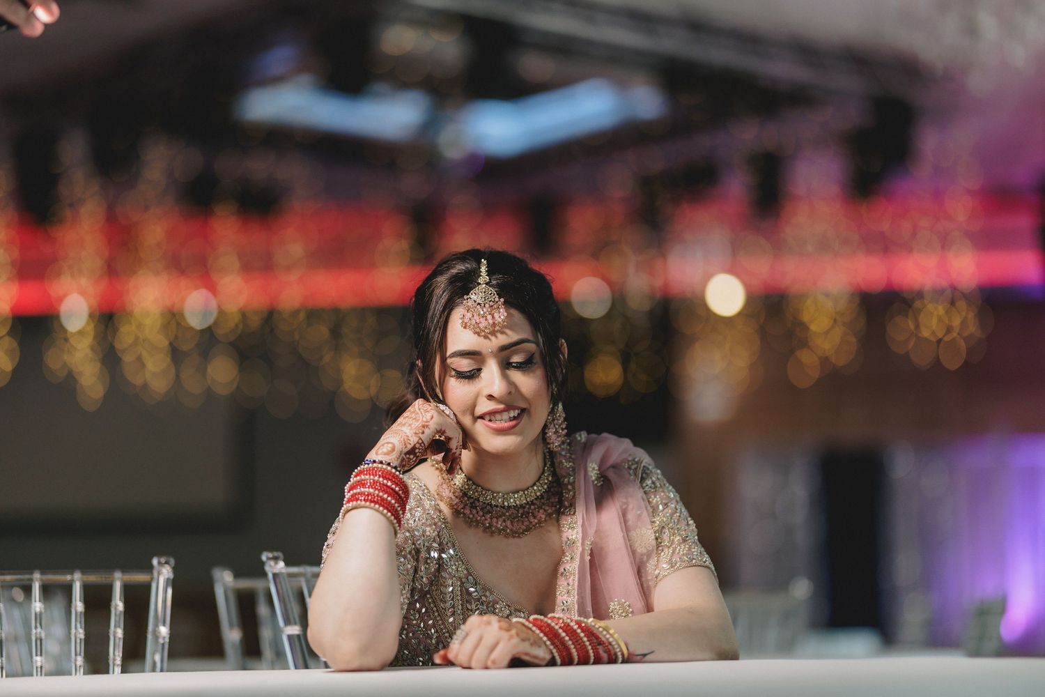 Wedding reception venue with soft pink lighting and hanging string lights creating a romantic atmosphere. Ring Ceremony Pose