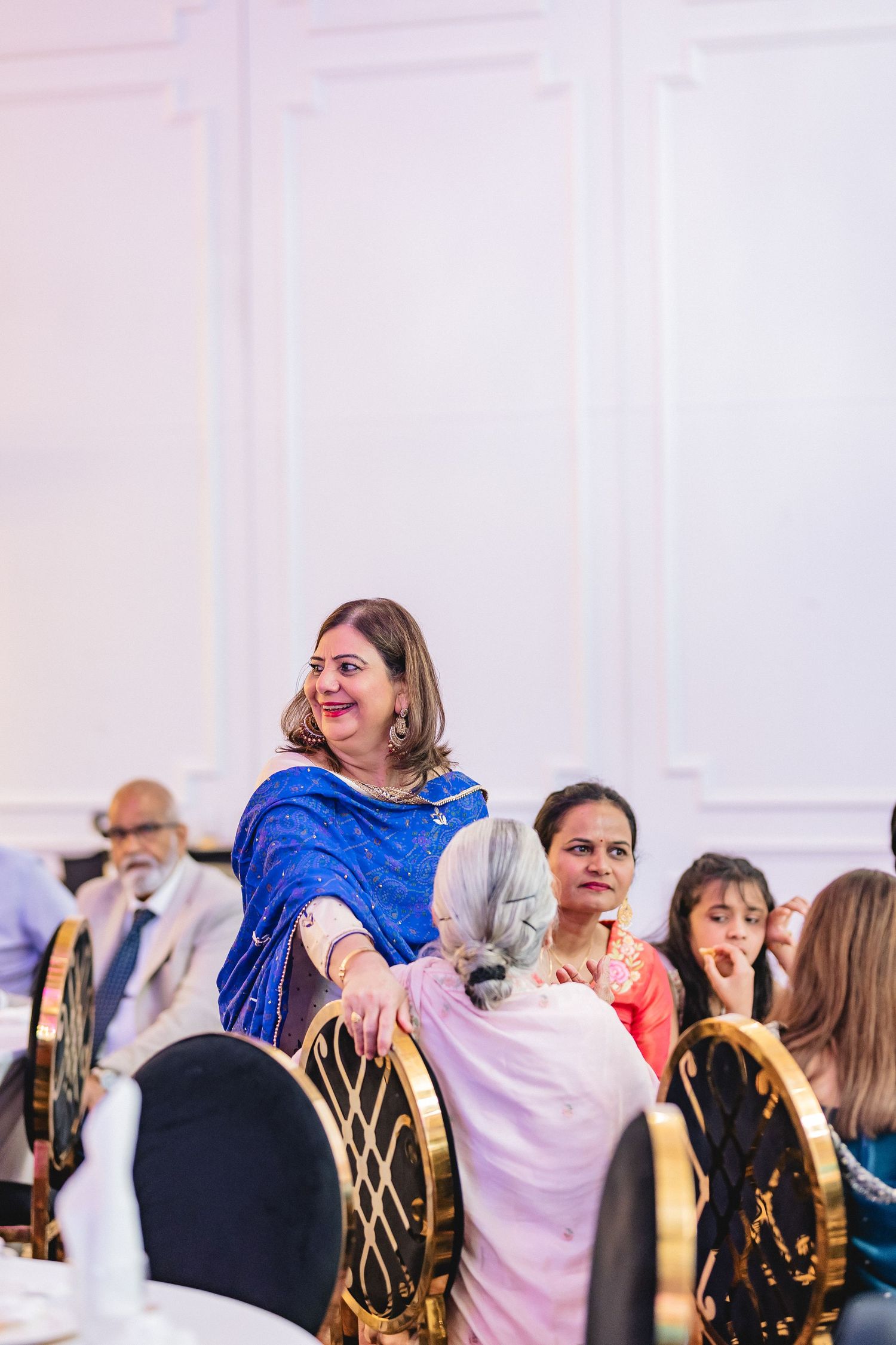 A group of wedding guests dancing and celebrating joyfully at a reception with someone in a bright blue dress.