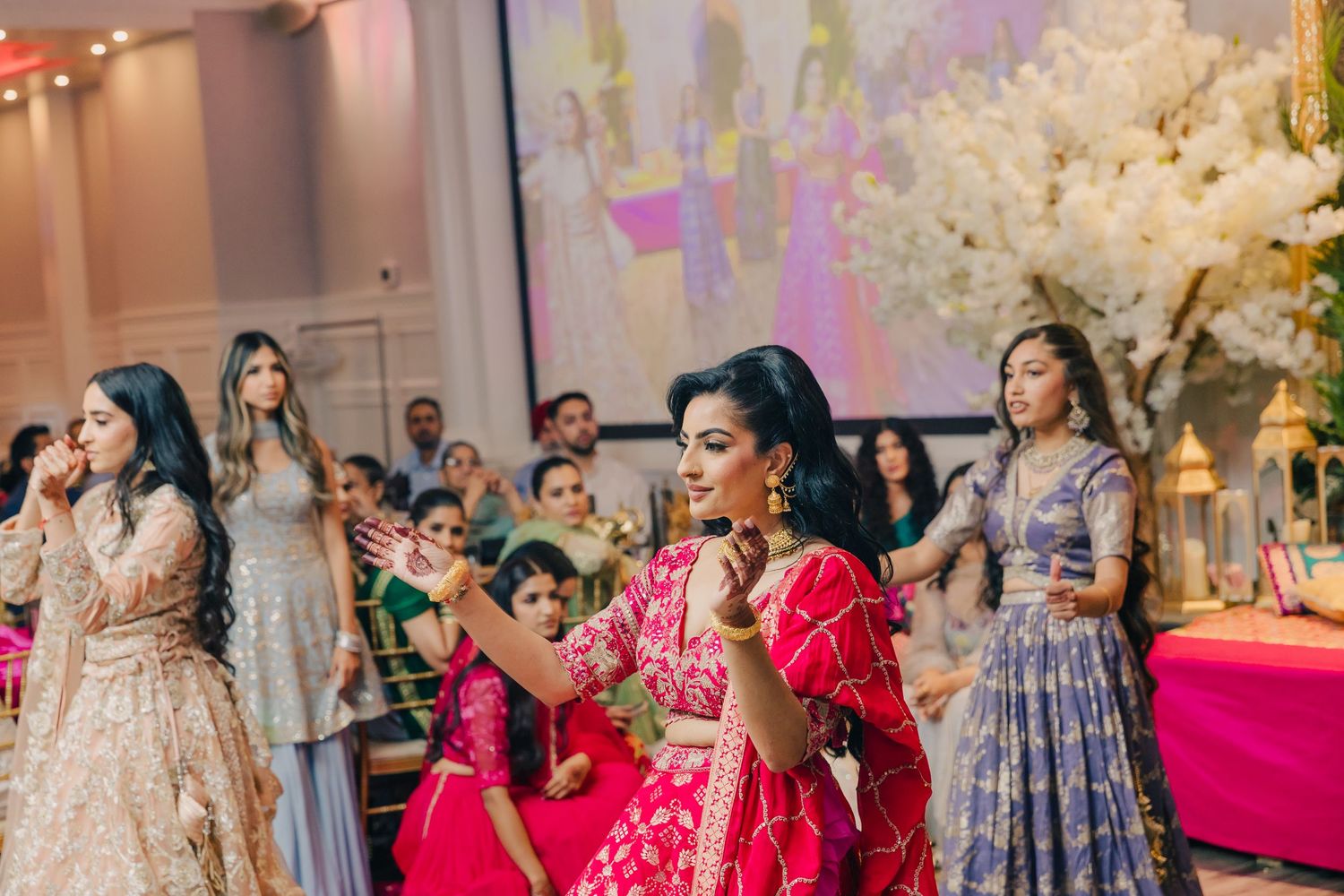 Guests in colorful traditional Indian attire celebrate during a wedding reception with white floral decorations.