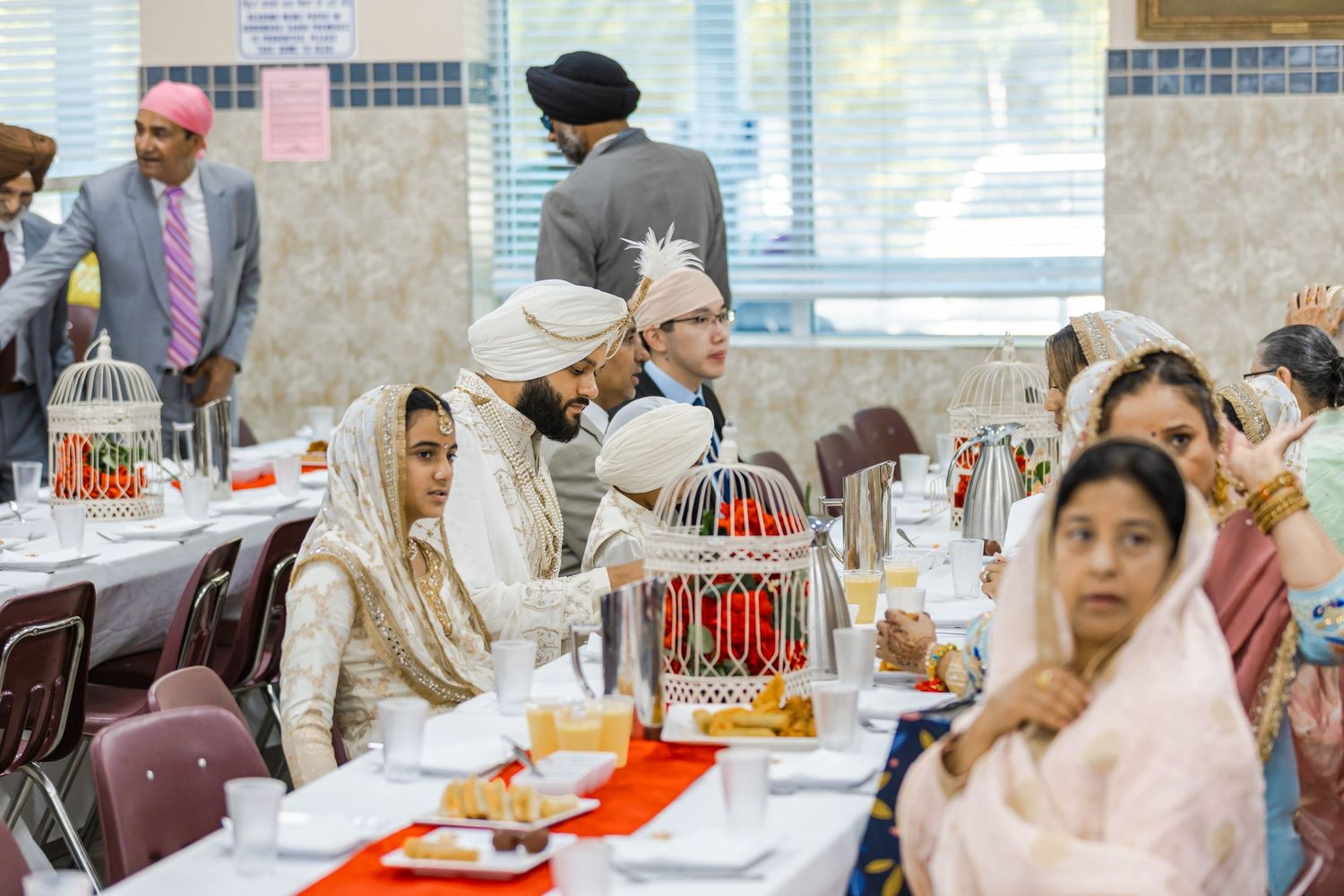 Indoor celebration with guests seated at decorated tables in traditional Indian formal wear.