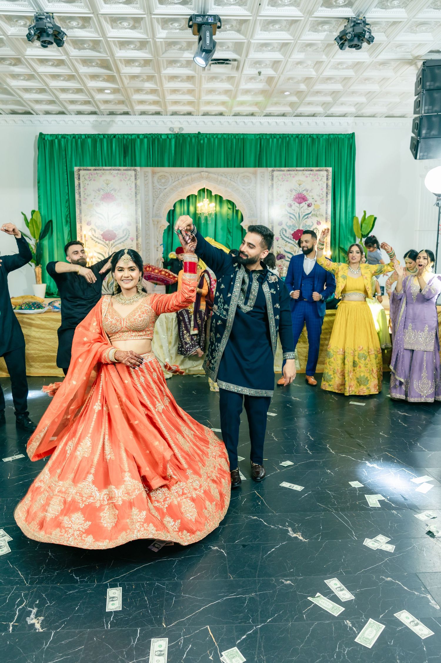 Wedding celebration with dancers in traditional attire performing on black marble floor. Red Lehnga on jaggo Night