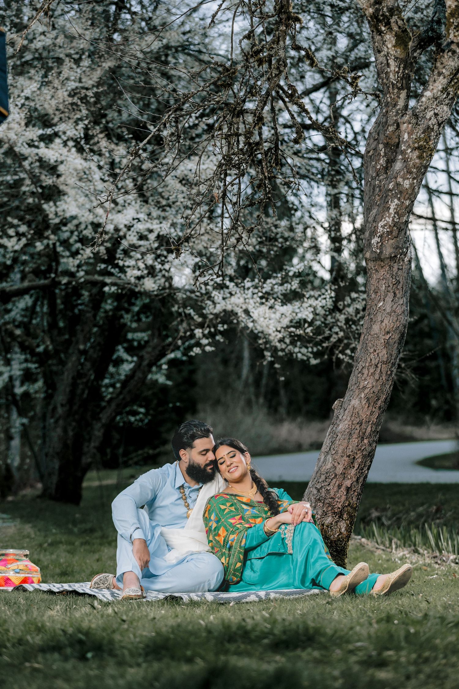 Couple relaxing on grass under flowering trees during a spring photoshoot.