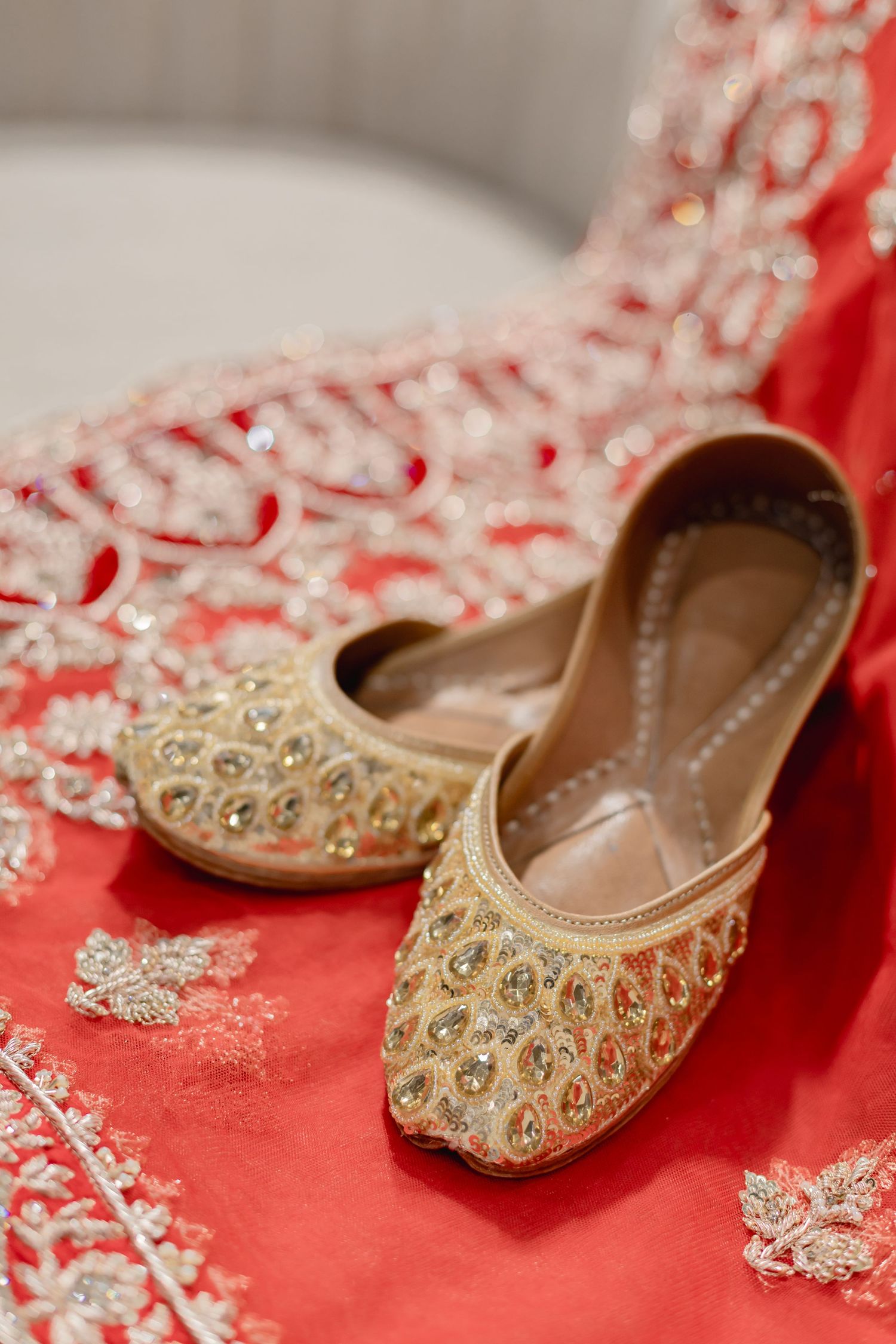 Gold embellished traditional Indian wedding shoes displayed on red embroidered fabric.