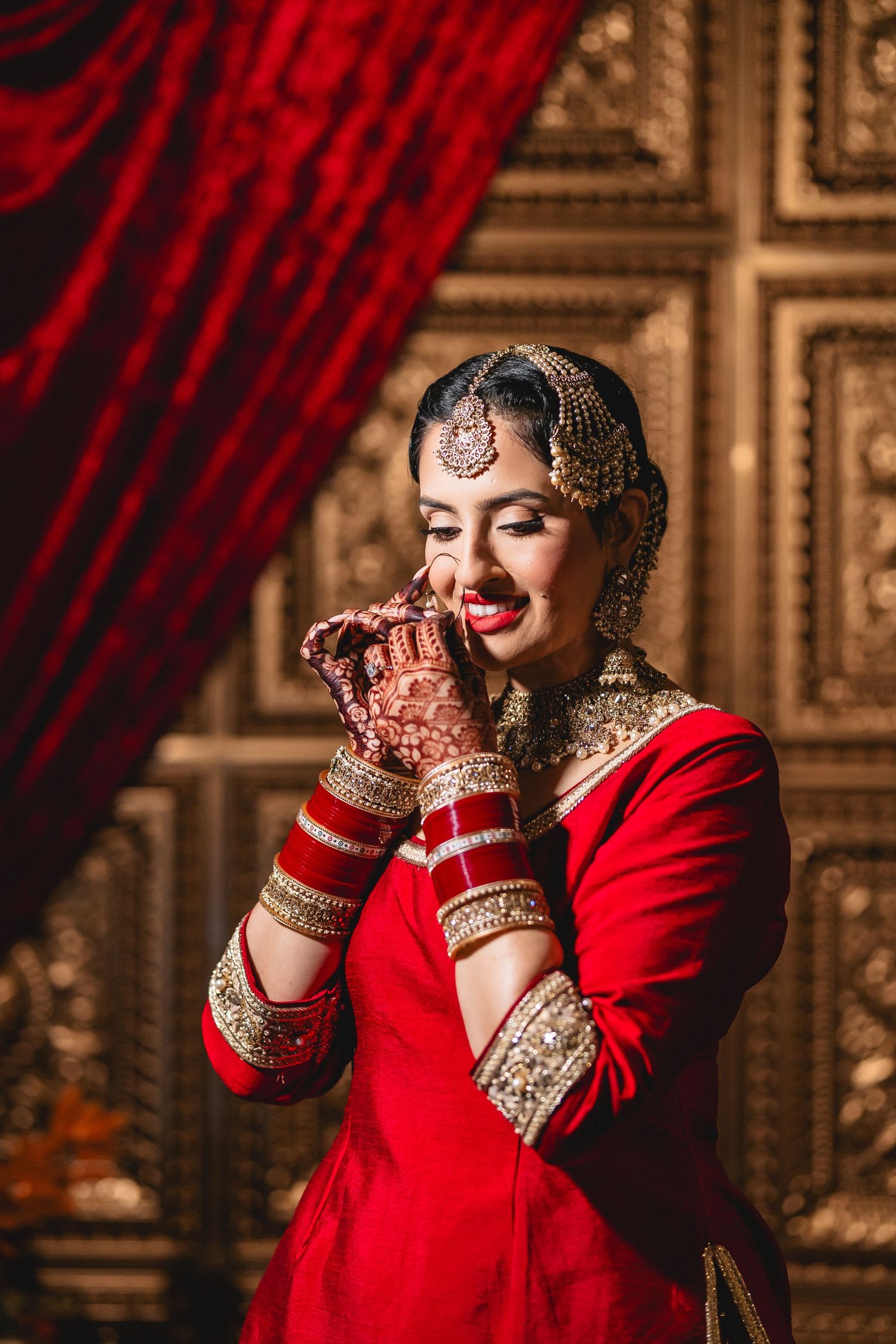 Traditional Indian bride in red attire with intricate henna designs and jewelry smiles during wedding ceremony.