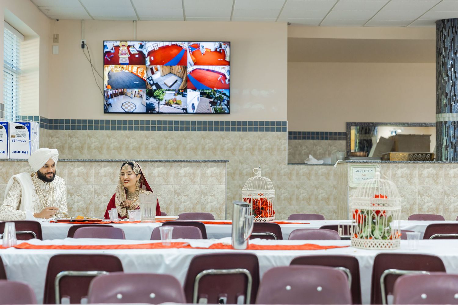 Cafeteria-style room with mounted TVs and rows of empty tables and chairs.